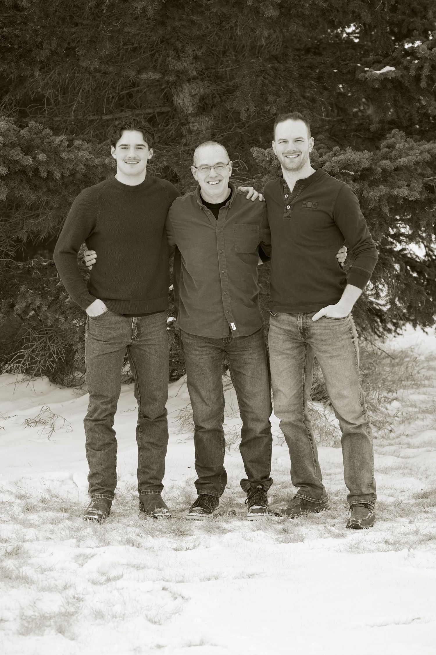 Three people stand together smiling in the snow wearing casual winter clothing in a black and white photo.