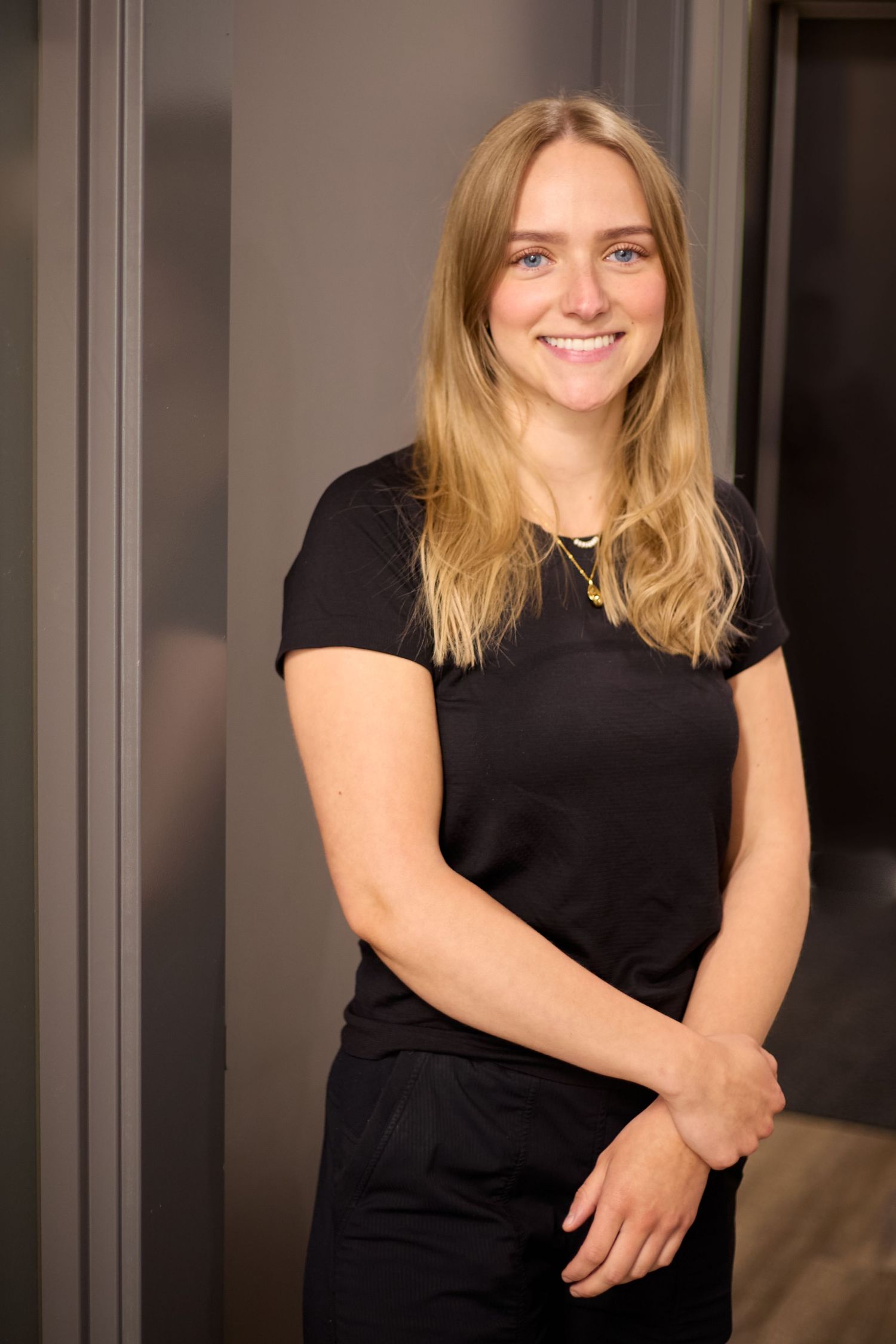 Massage therapist in black shirt smiling warmly in professional indoor setting.