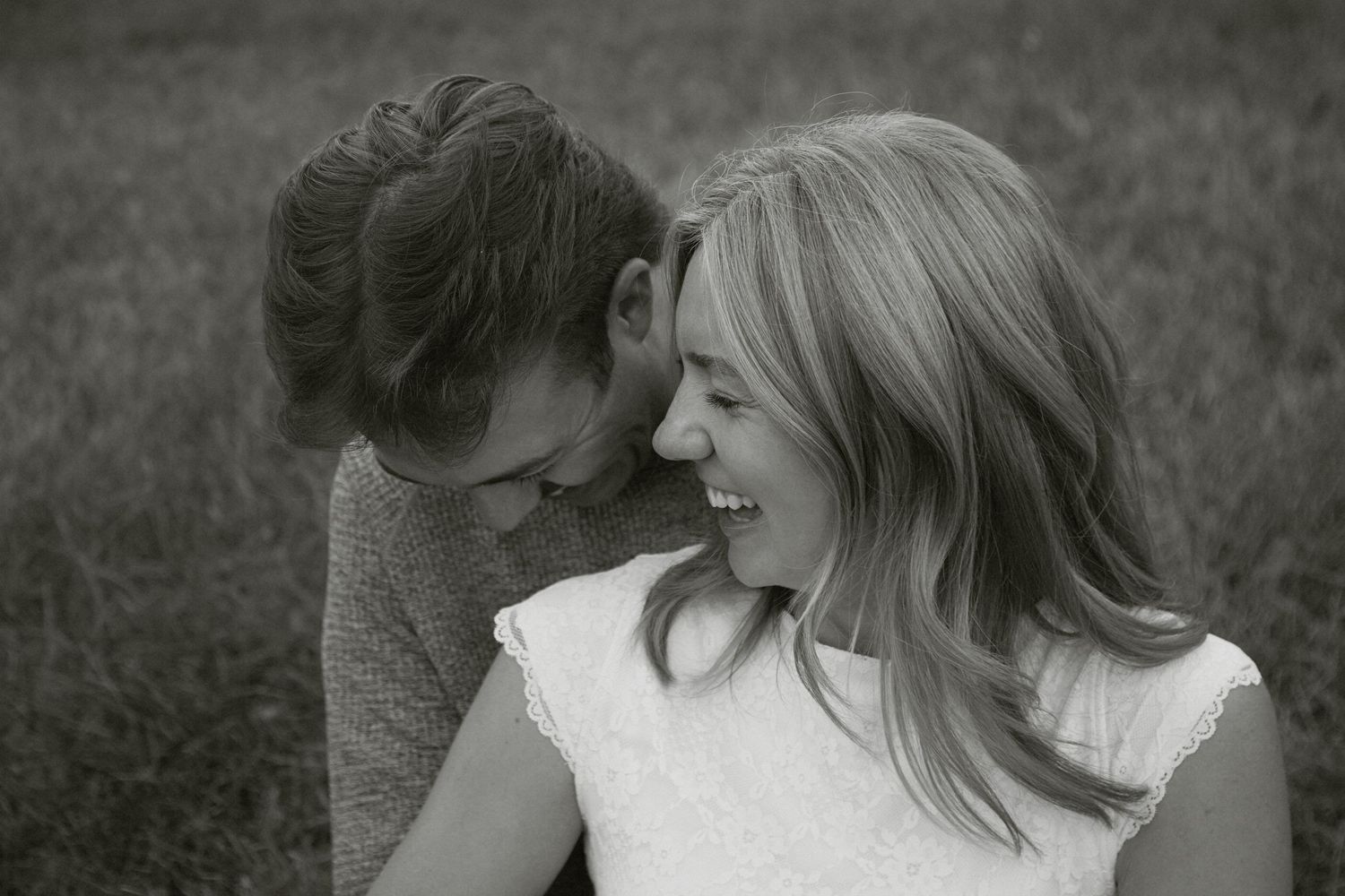 Black and white photo of two women laughing and sharing a joyful moment outdoors in a field.