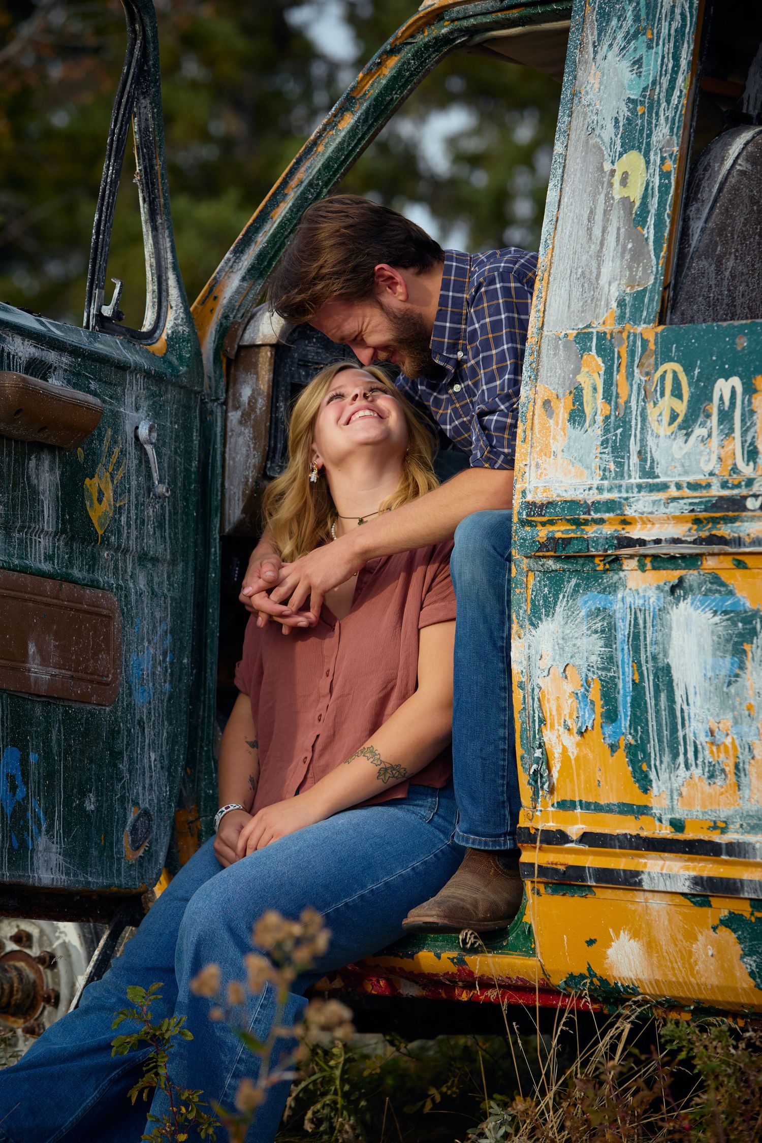 Couple sharing a romantic moment in an old rustic truck with peeling blue and yellow paint during golden hour.