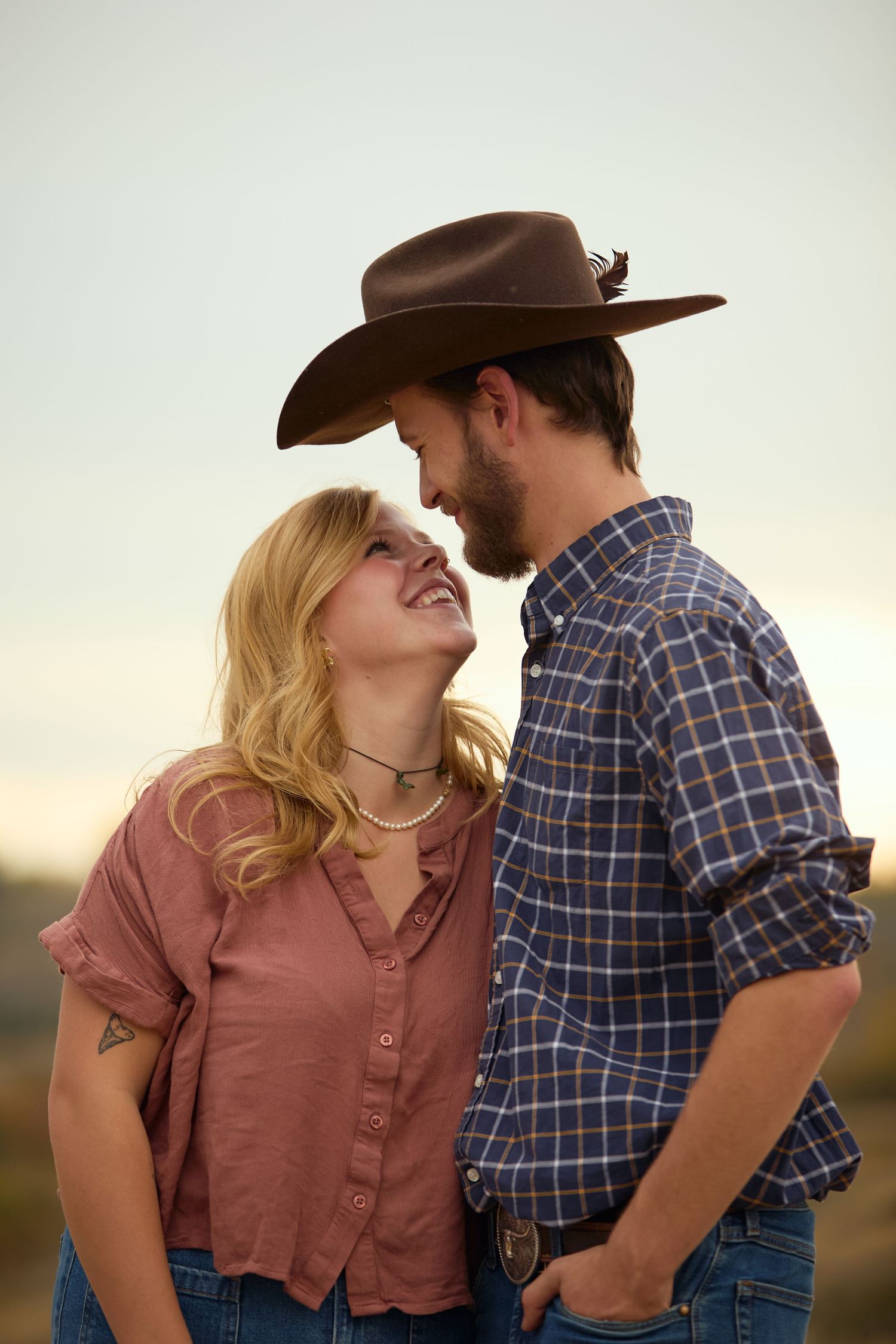 A couple in western attire share intimate moments in a romantic outdoor photo series at sunset.