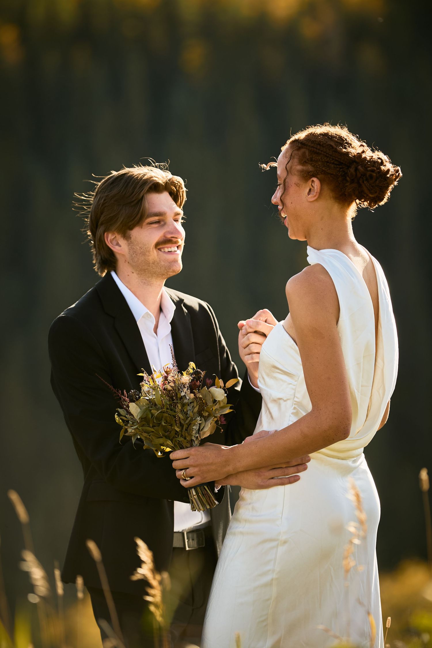 A happy couple embraces and laughs together during their outdoor wedding ceremony at sunset.