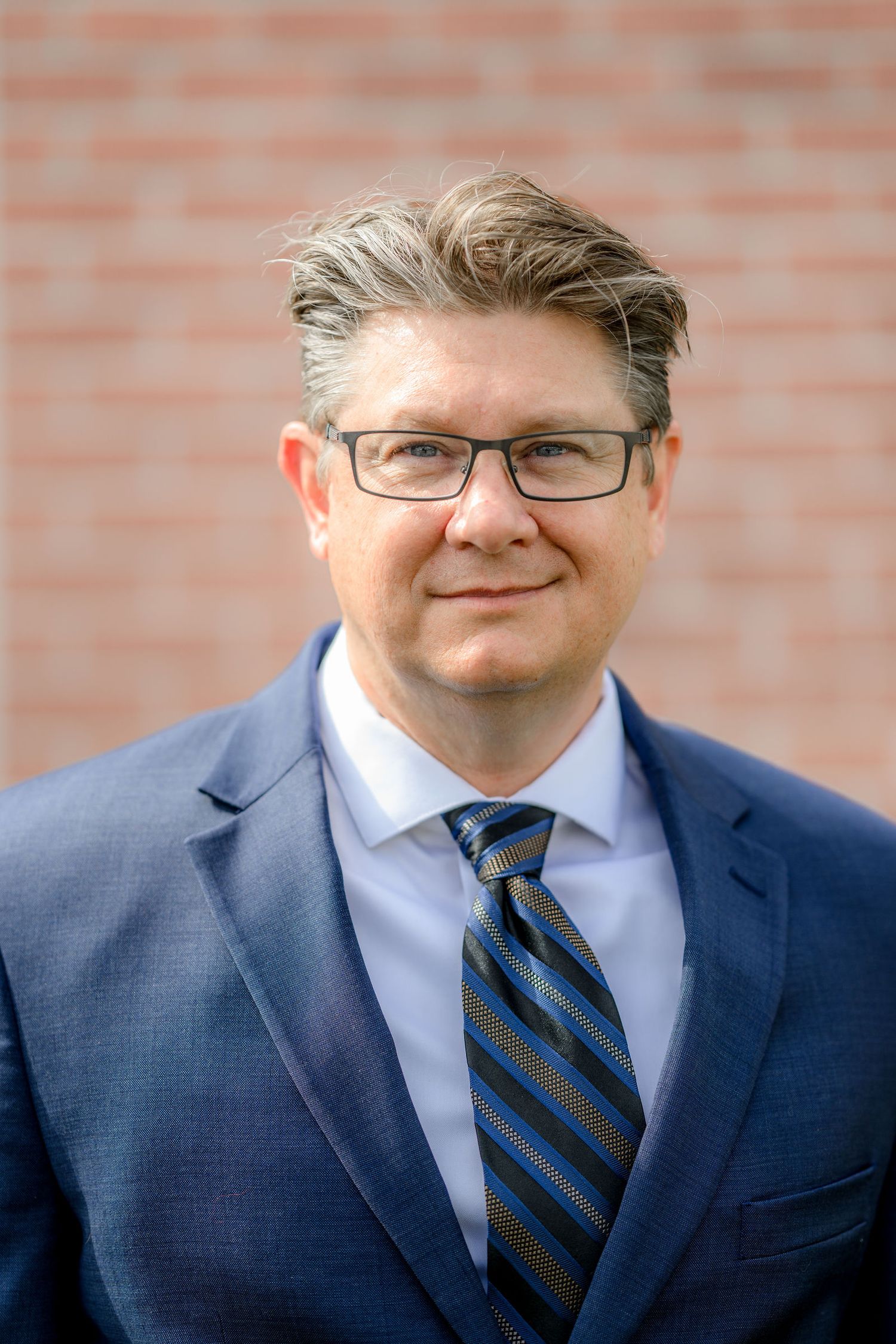 Matthew in a formal blue suit and glasses during his headshot photoshoot at his home in San Diego, ca,