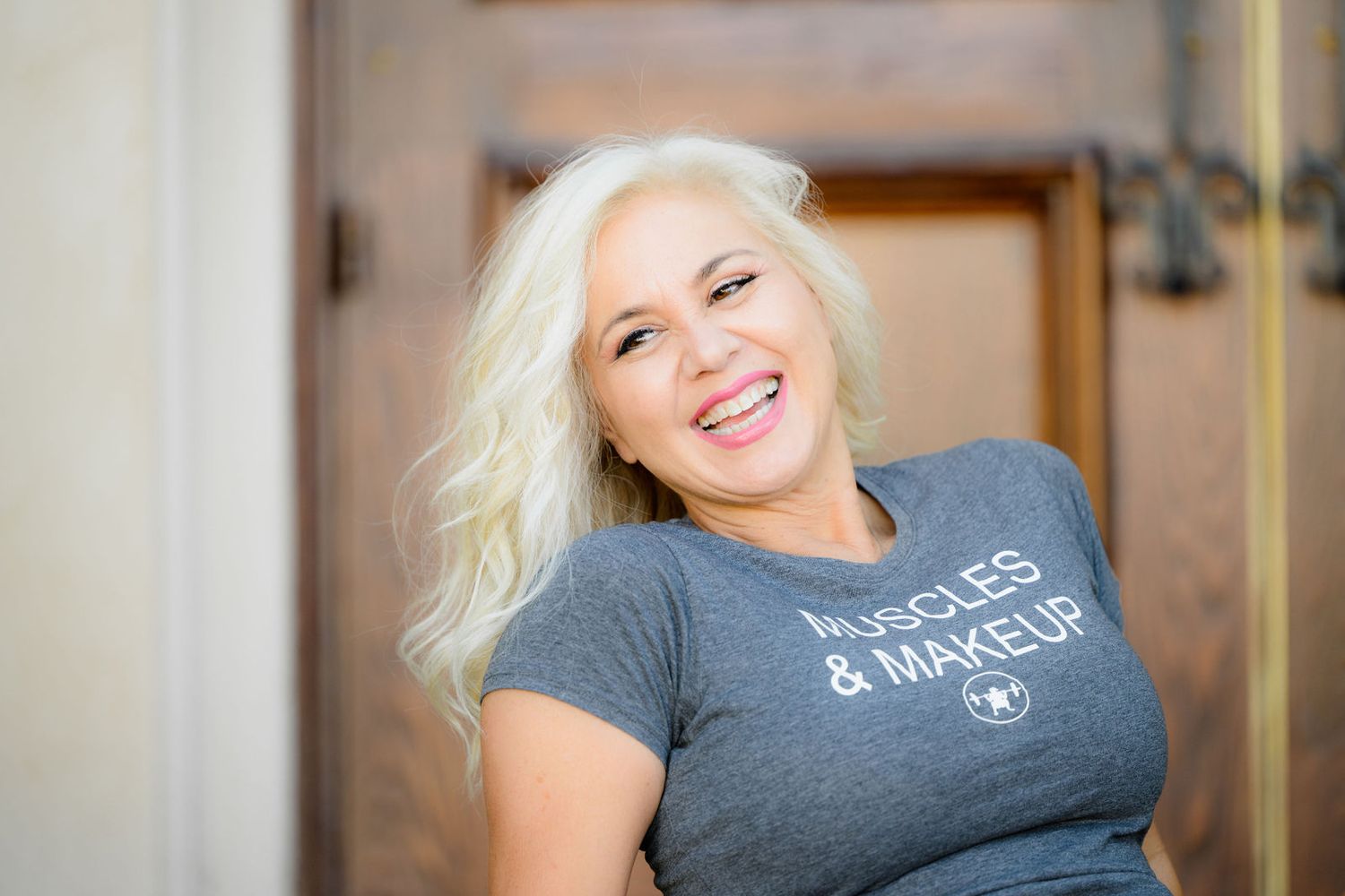 Lisa at Balboa Park in San Diego posing for her personal branding photoshoot wearing a muscles and make up shirt and smiling proudly.
