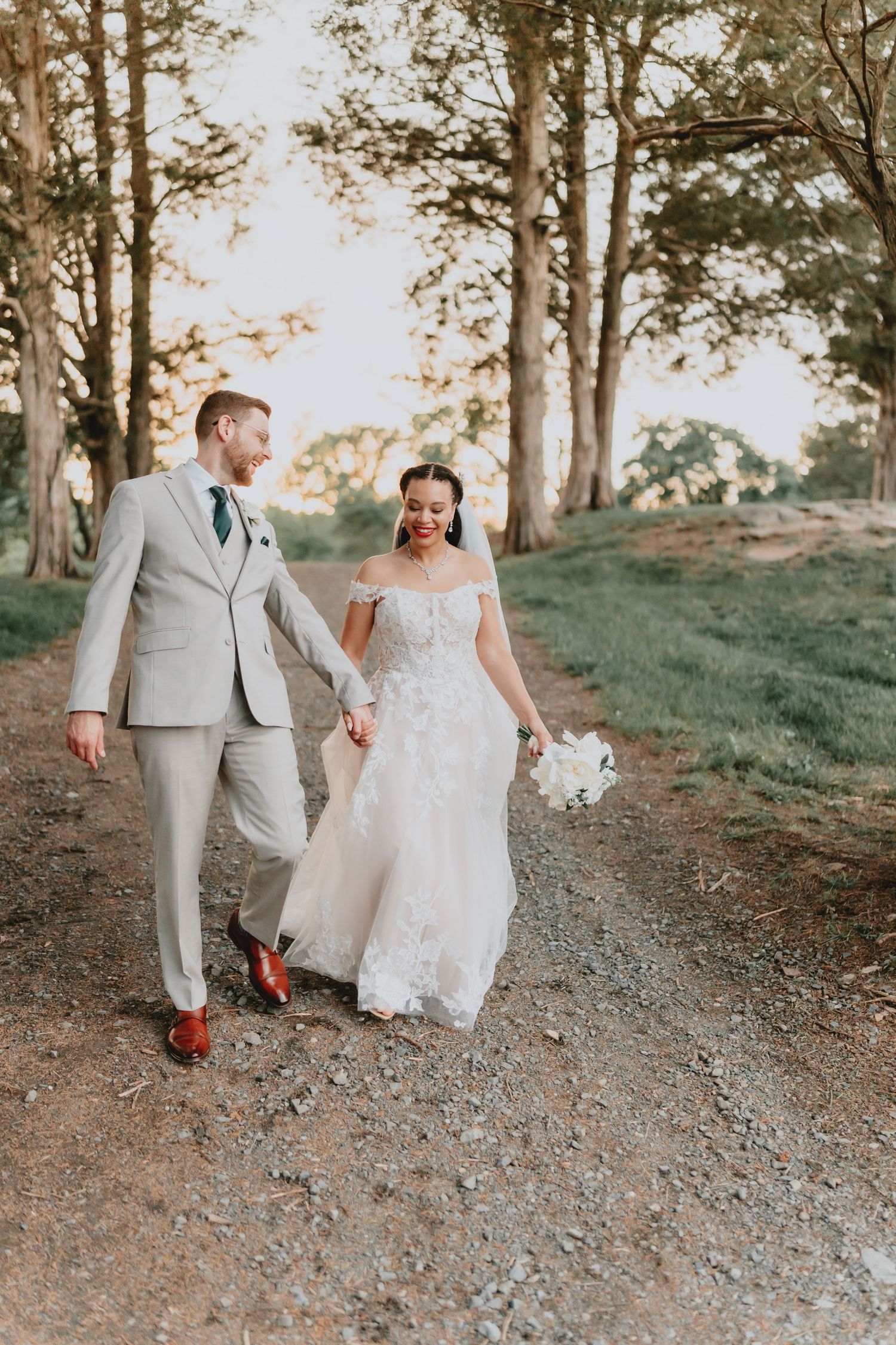 A couple walking along a rustic forest path in wedding attire.