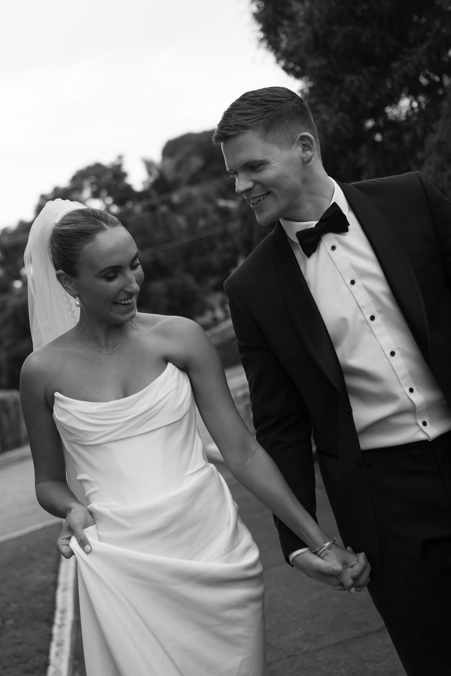 A series of candid black and white wedding photos showing a couple laughing together outdoors in formal attire.