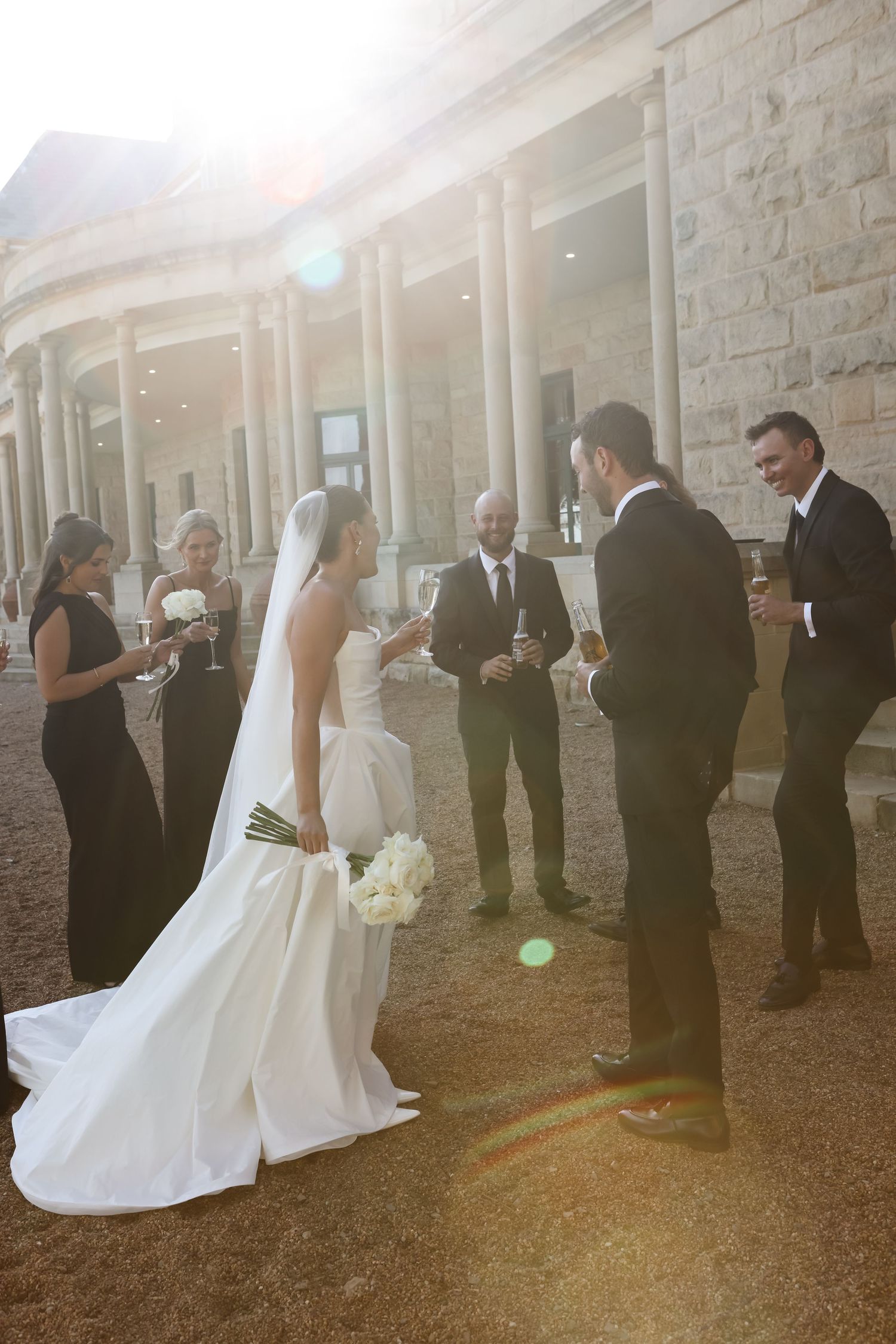 Wedding party lines up against stone wall for formal photos during sunset ceremony.