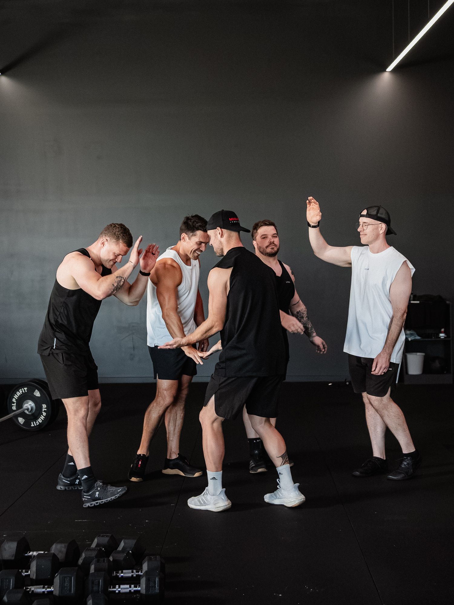 Group of men in athletic wear sharing a lighthearted moment during gym workout.