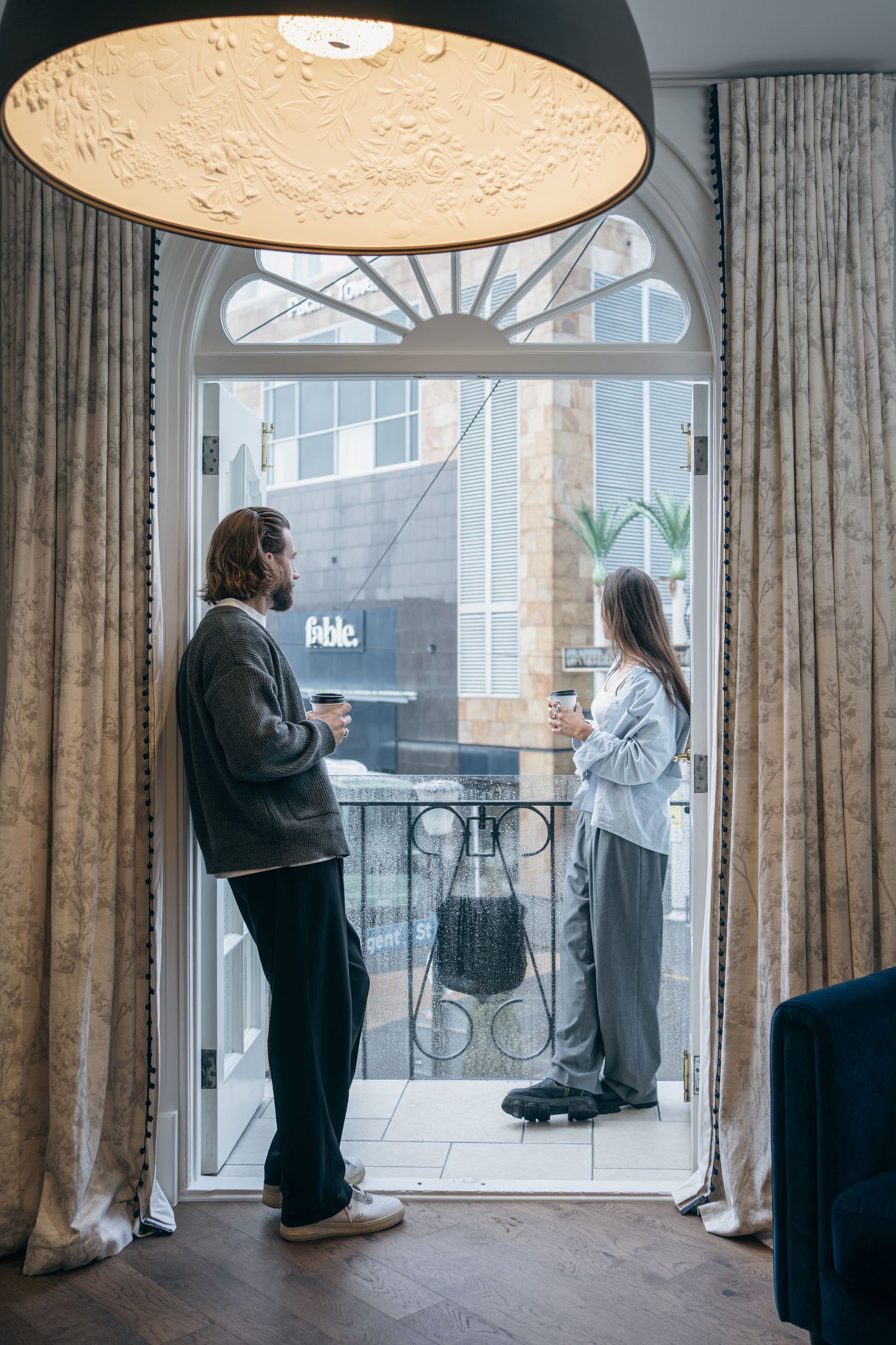 Two people having conversation on balcony with arched window and decorative ceiling light.