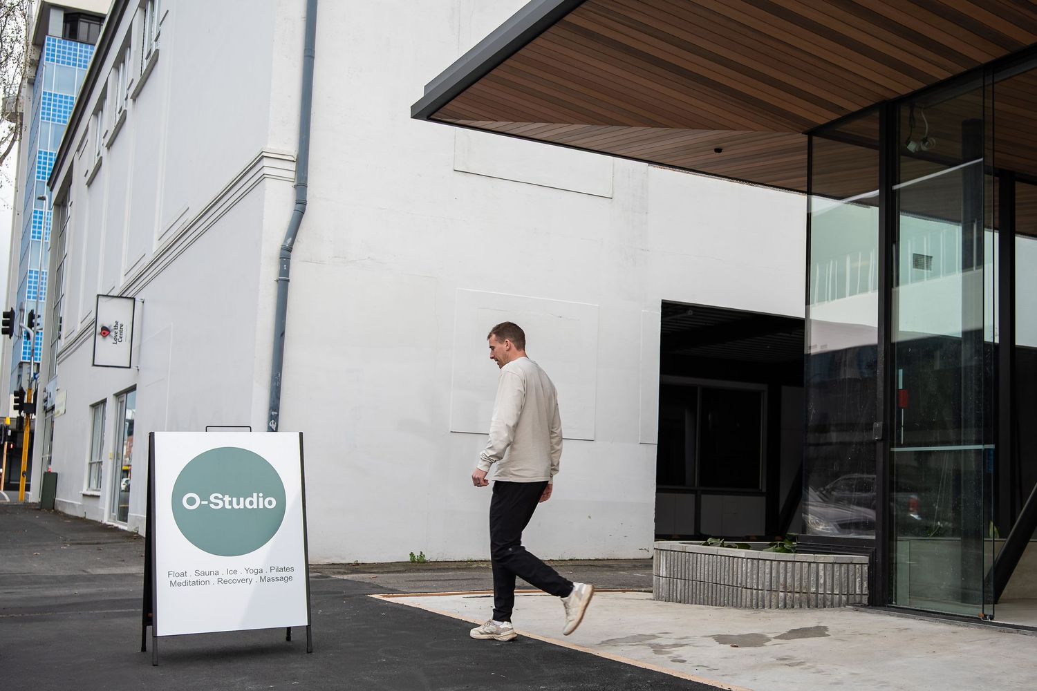 A person in business attire walks past a modern white building exterior with glass windows and architectural details.