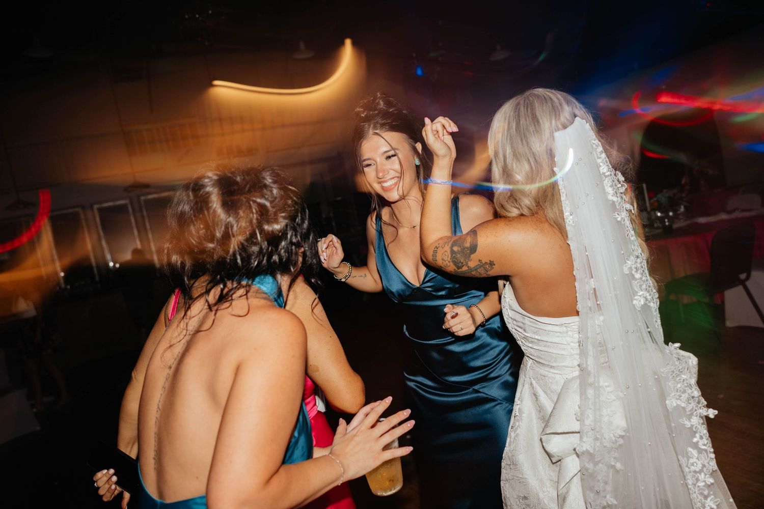 Bride dances joyfully with guests in blue dresses at lively wedding reception.