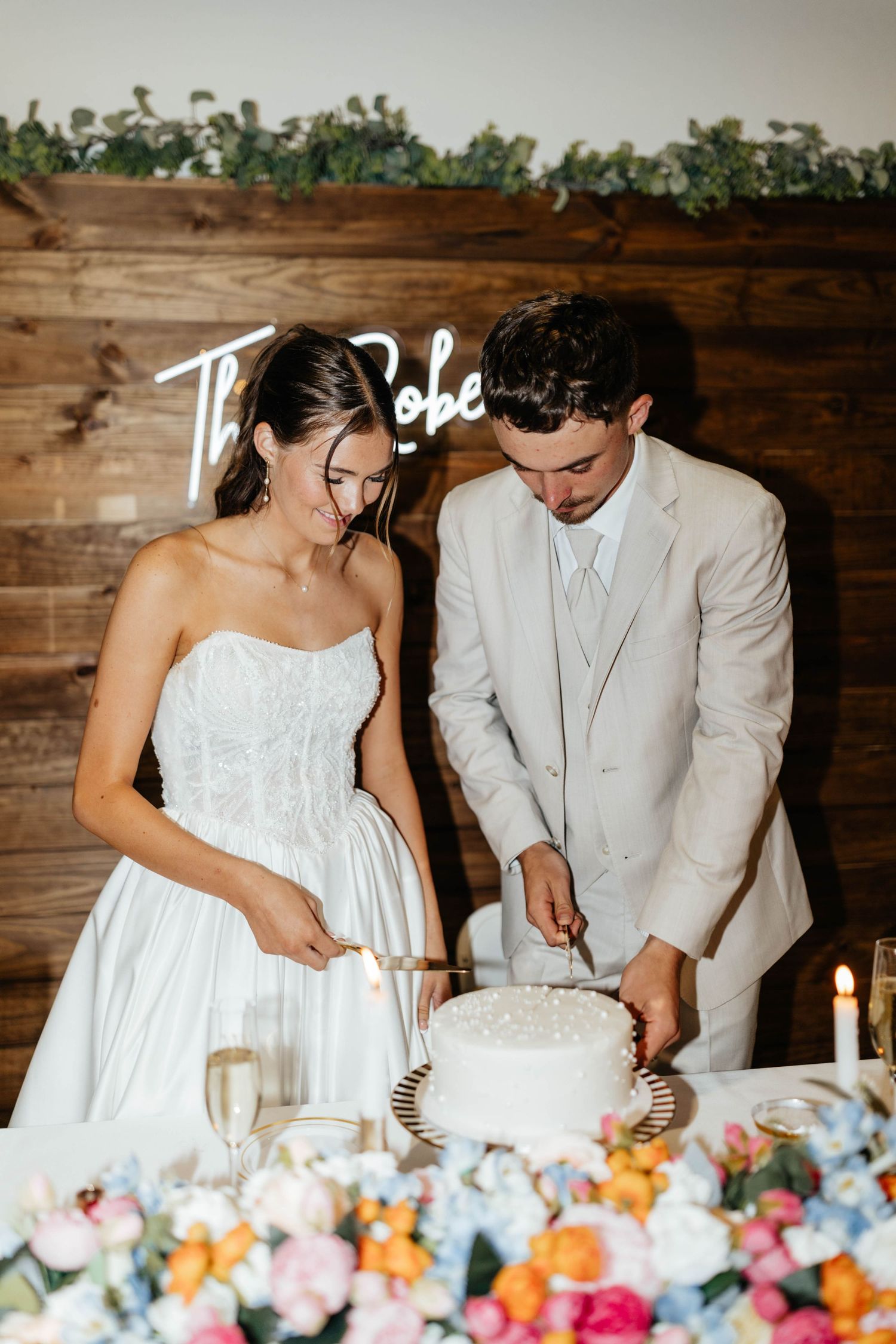 Bride and groom cut their white wedding cake in front of a rustic wood backdrop.