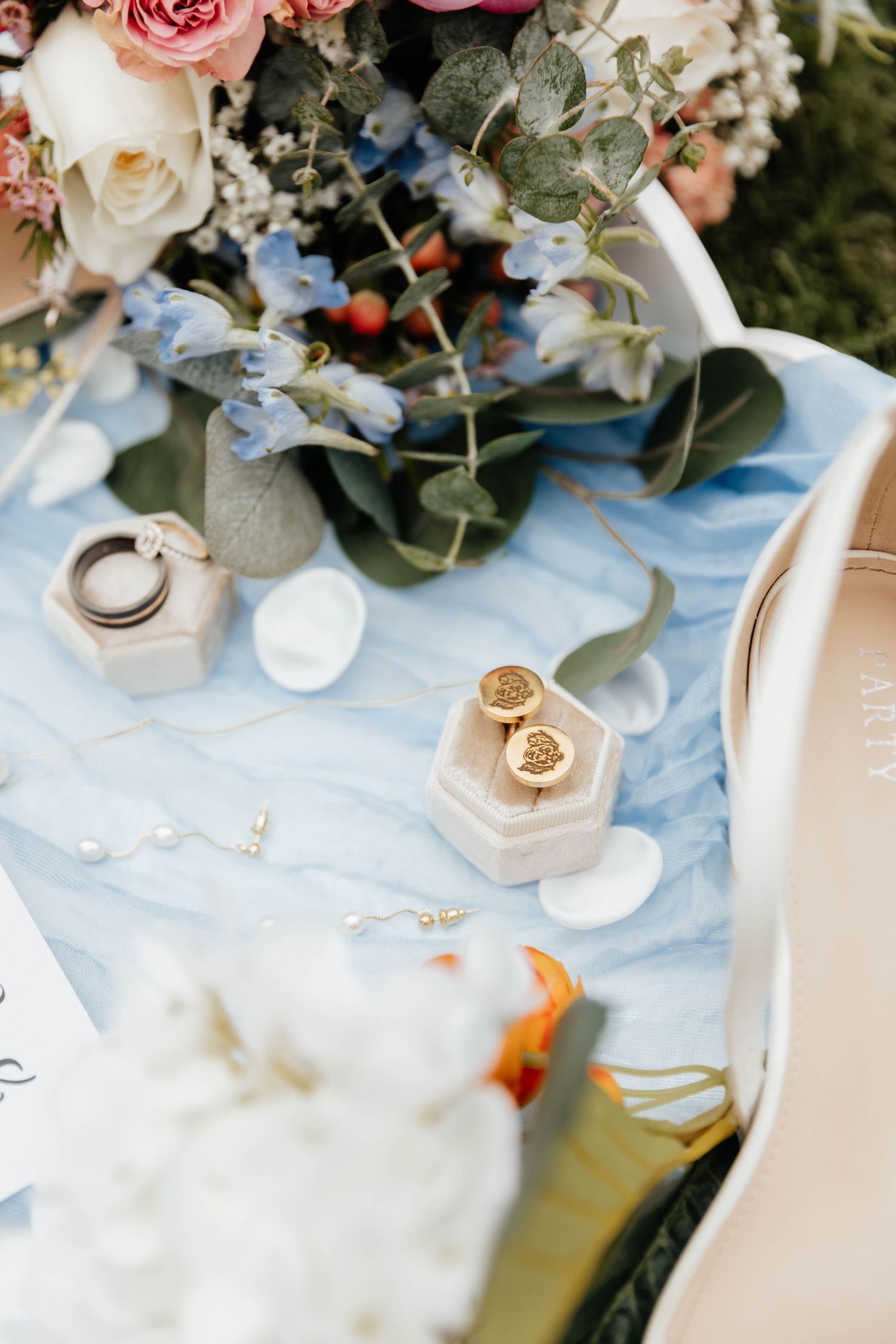 Wedding flat lay featuring gold cufflinks in a velvet box, rings, and floral bouquet.