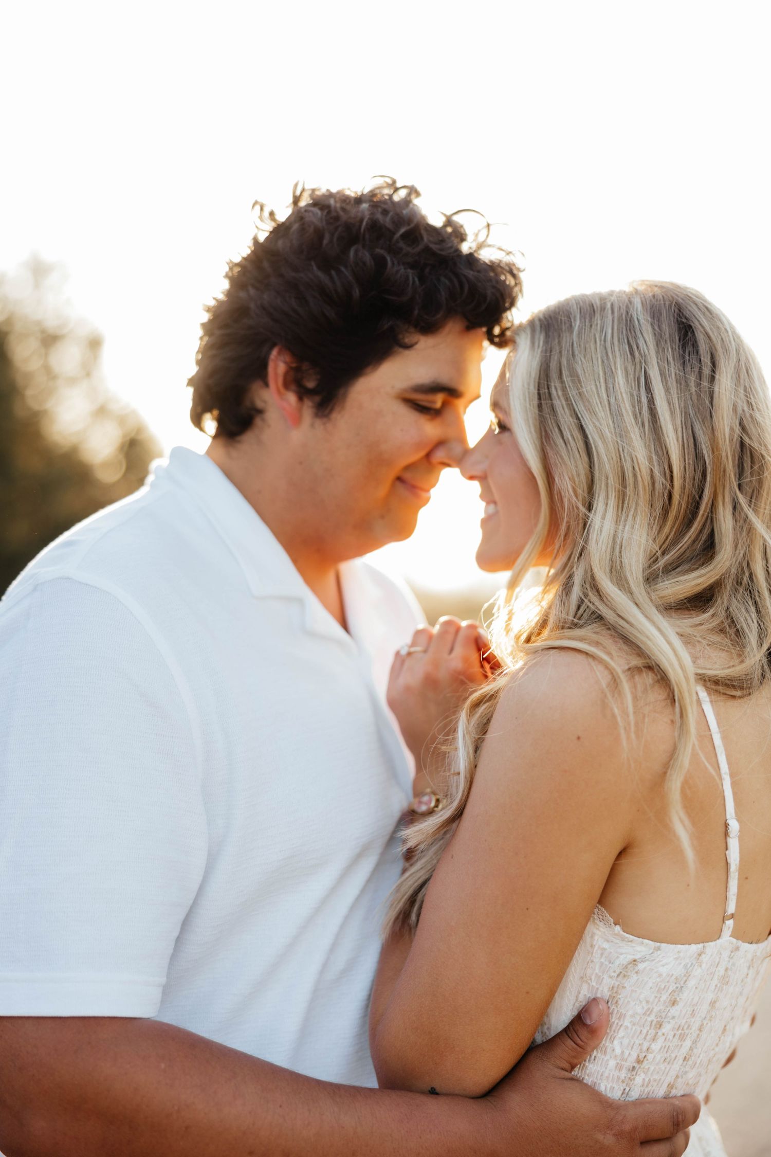 Romantic couple about to kiss in warm golden sunlight during outdoor engagement session.