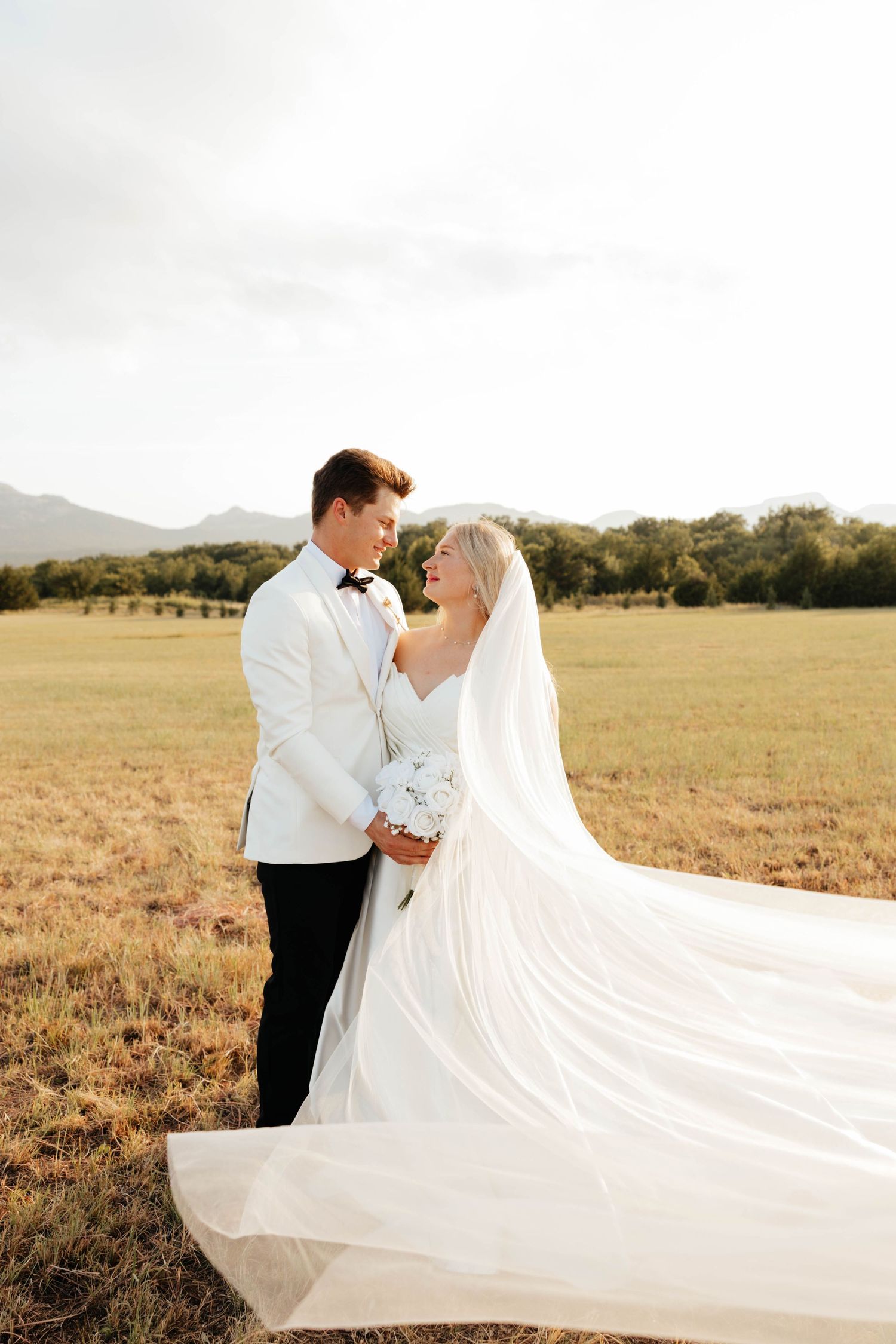 Bride and groom share a romantic moment in a golden field with mountains in the background.
