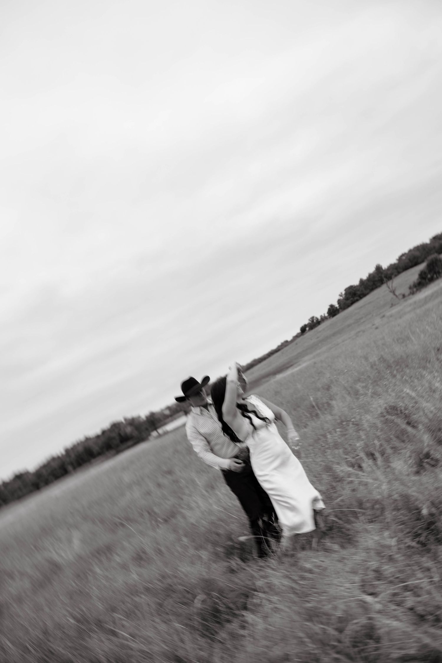 Black and white photo of couple dancing and kissing in an open field, man wearing cowboy hat.