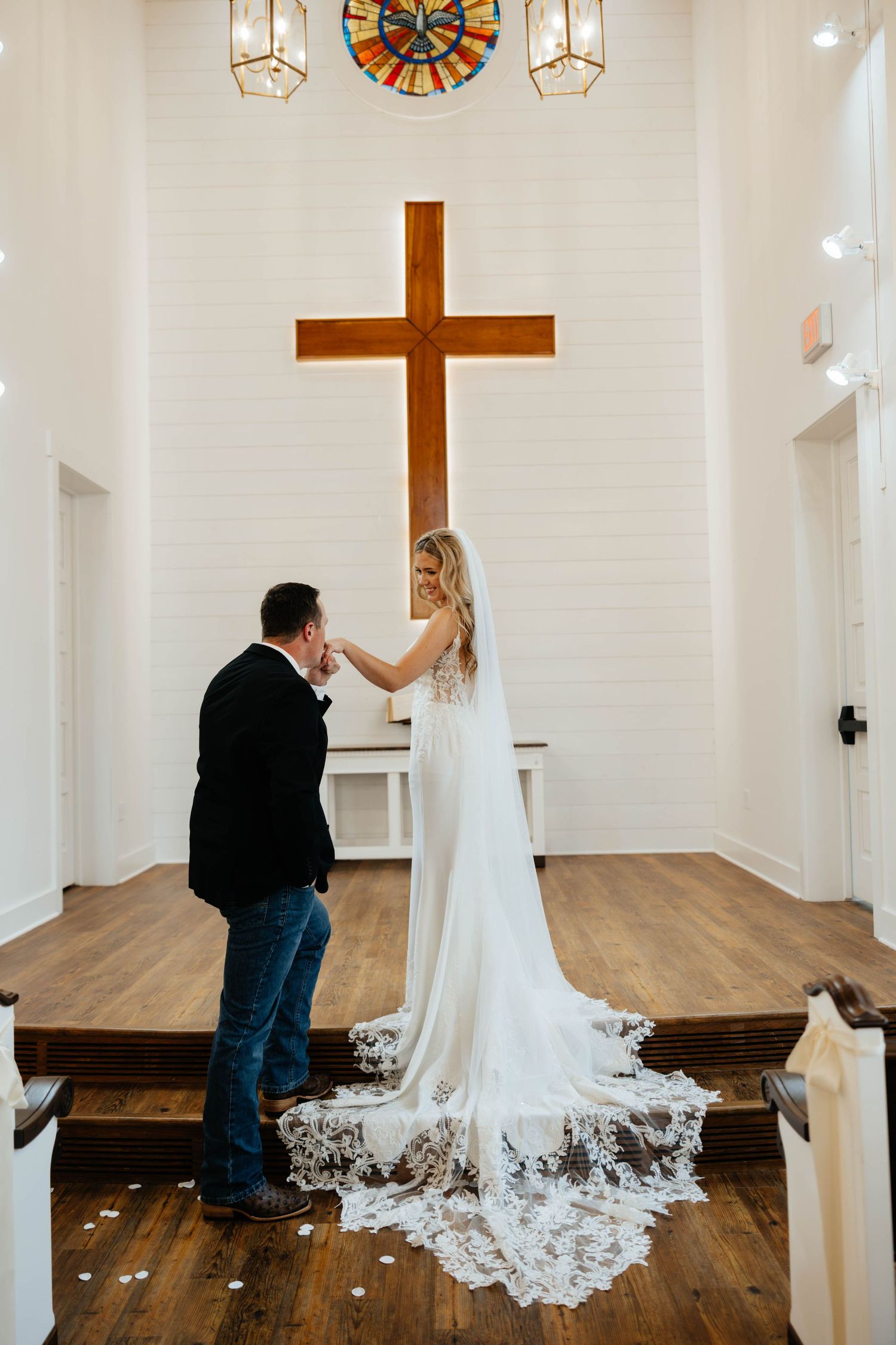 Bride and groom sharing first look moment inside white chapel with wooden cross and stained glass.