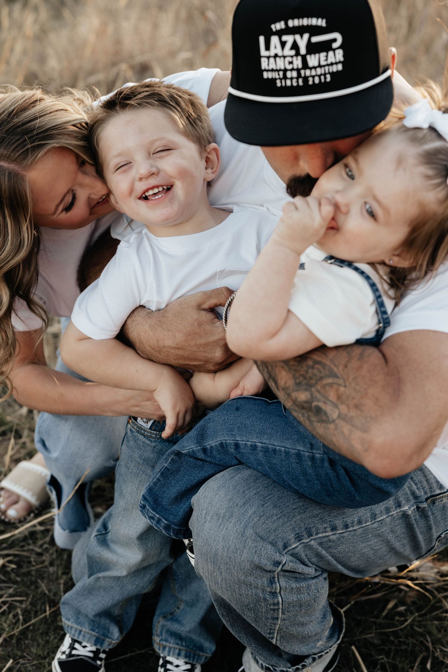 Happy family with two young children laughing together in a golden grass field.