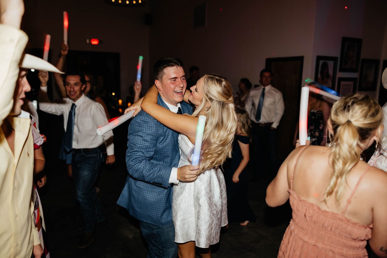 Bride and groom dancing joyfully with guests holding glow sticks at a lively wedding reception.