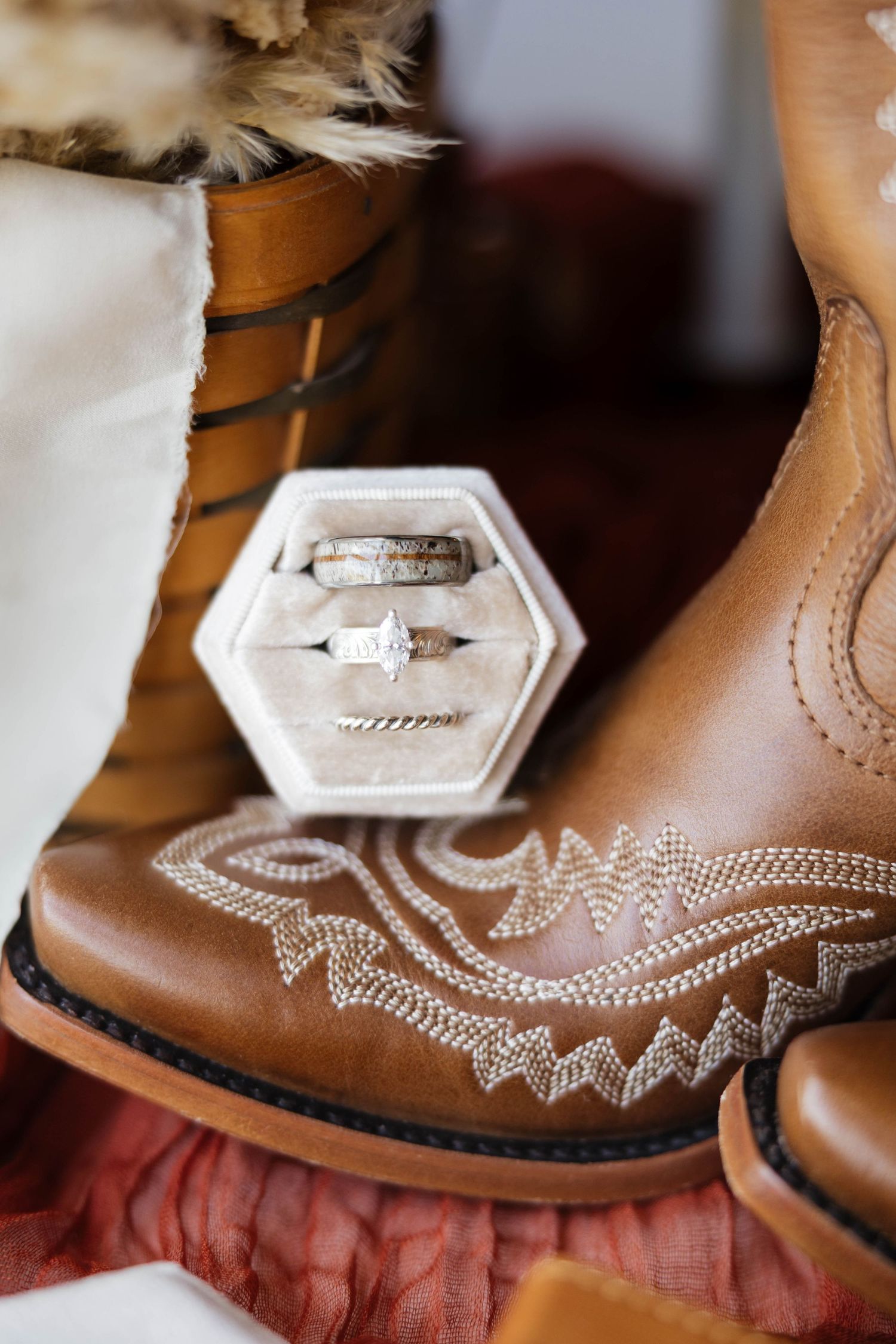 Wedding rings displayed in velvet hexagon box resting on tan embroidered cowboy boots.