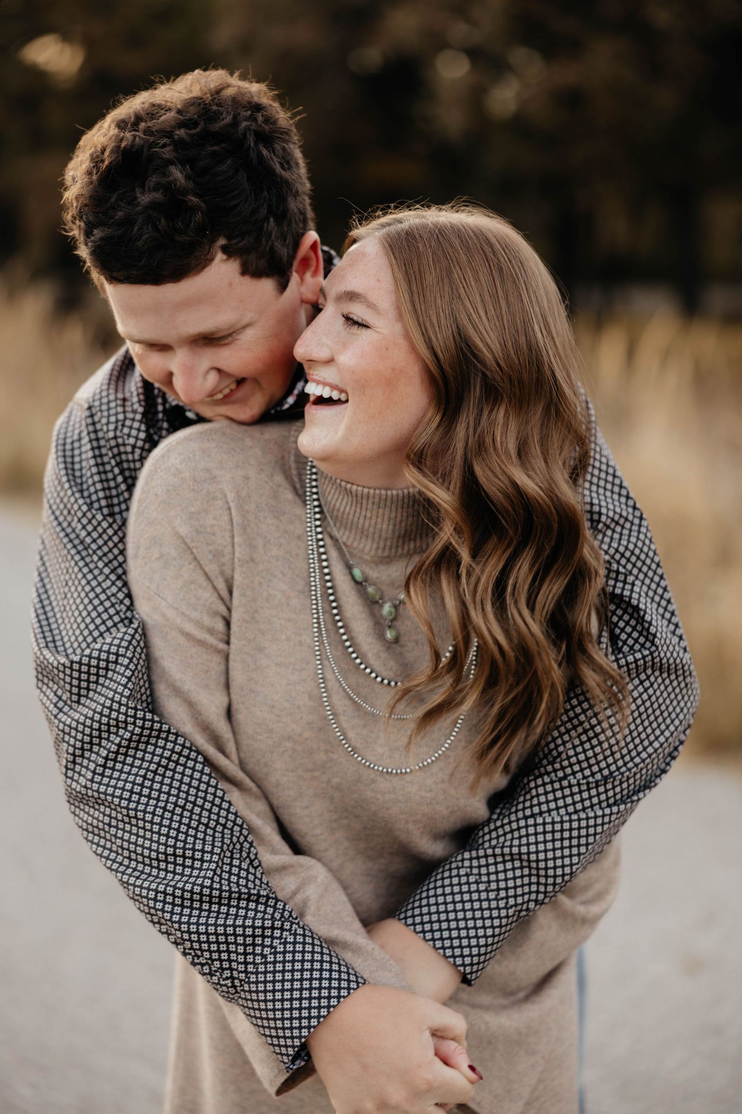 Happy couple embracing and laughing outdoors in autumn, woman wearing turtleneck and layered necklaces.