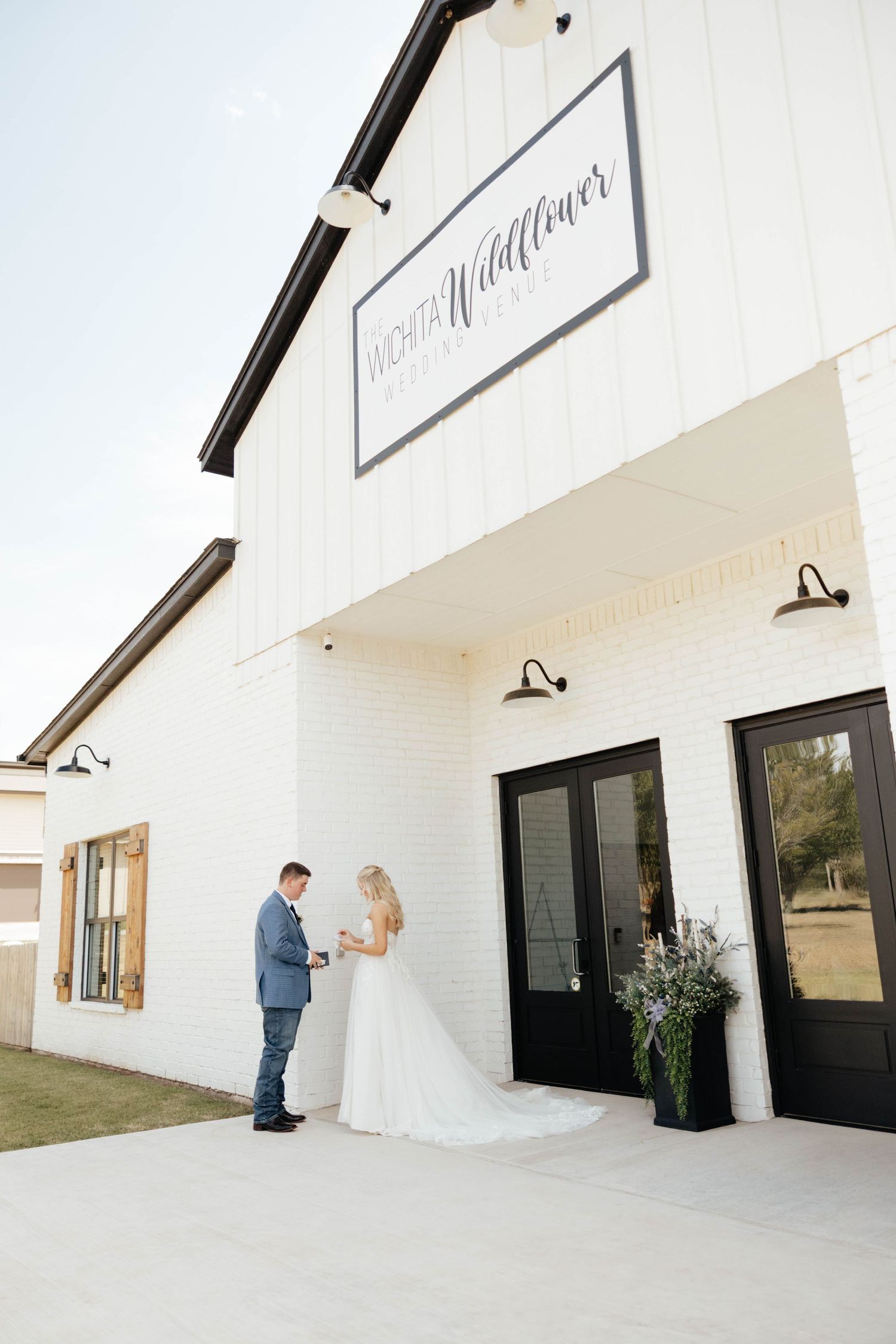 Bride and groom sharing first look outside white Wichita Wildflower wedding venue with black trim doors.