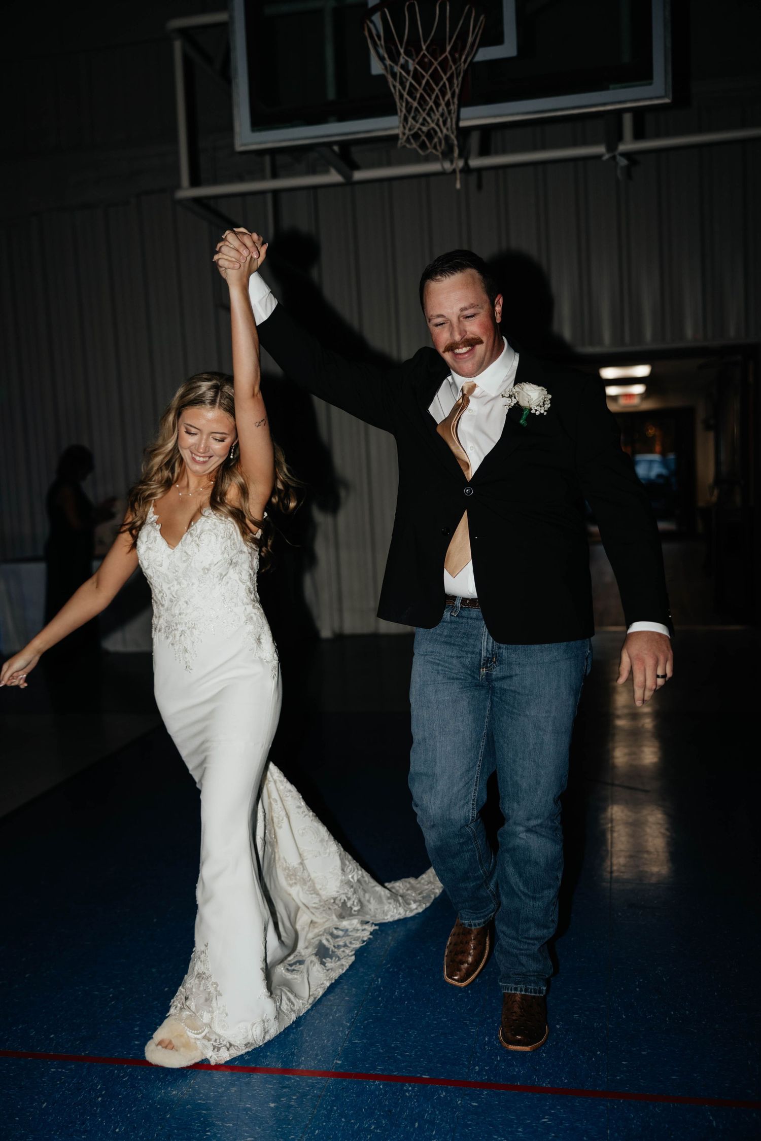Bride and groom making grand entrance onto dance floor at wedding reception in gymnasium venue.