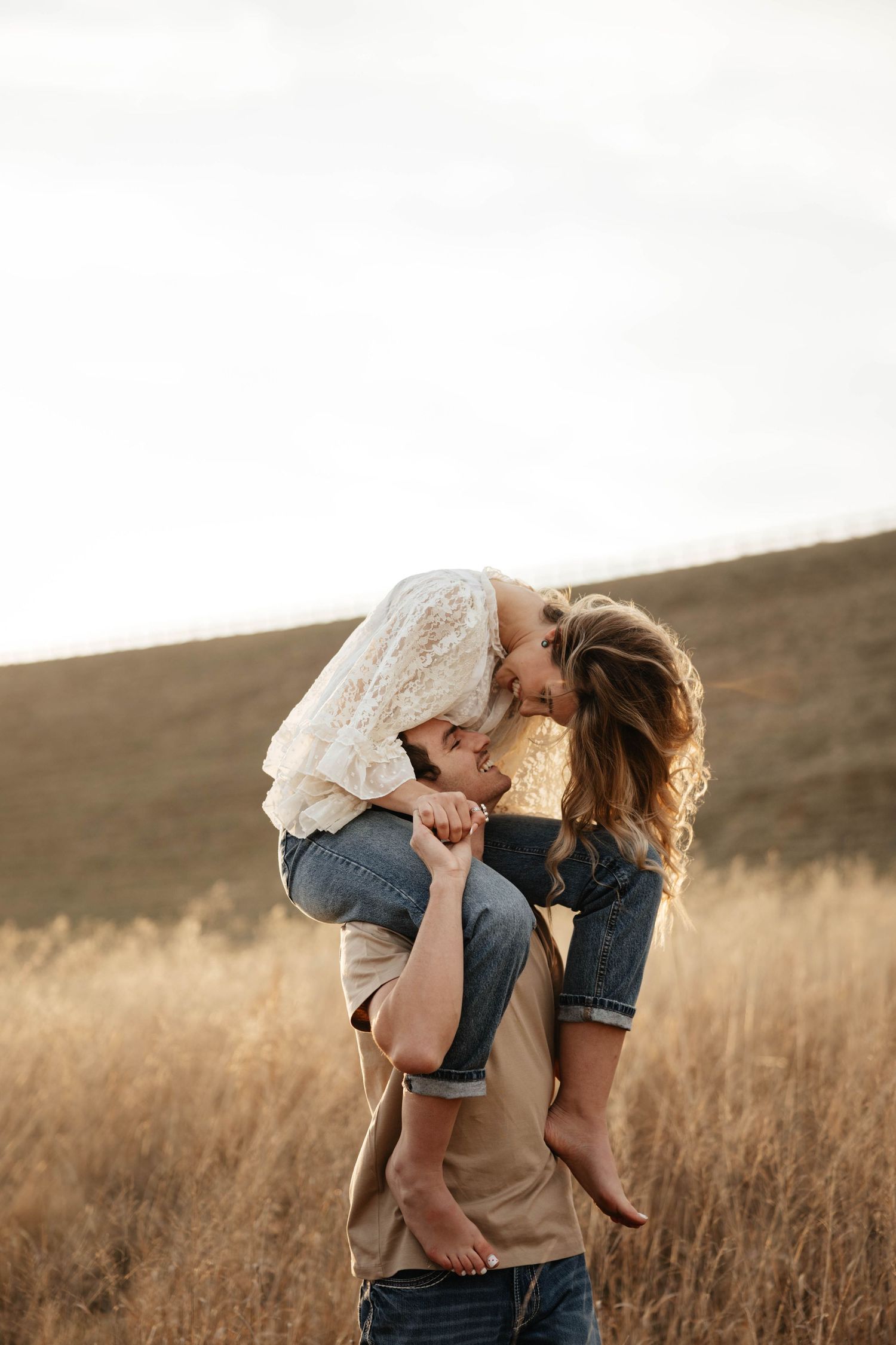 Man lifting woman on his shoulders for a kiss in a golden wheat field.