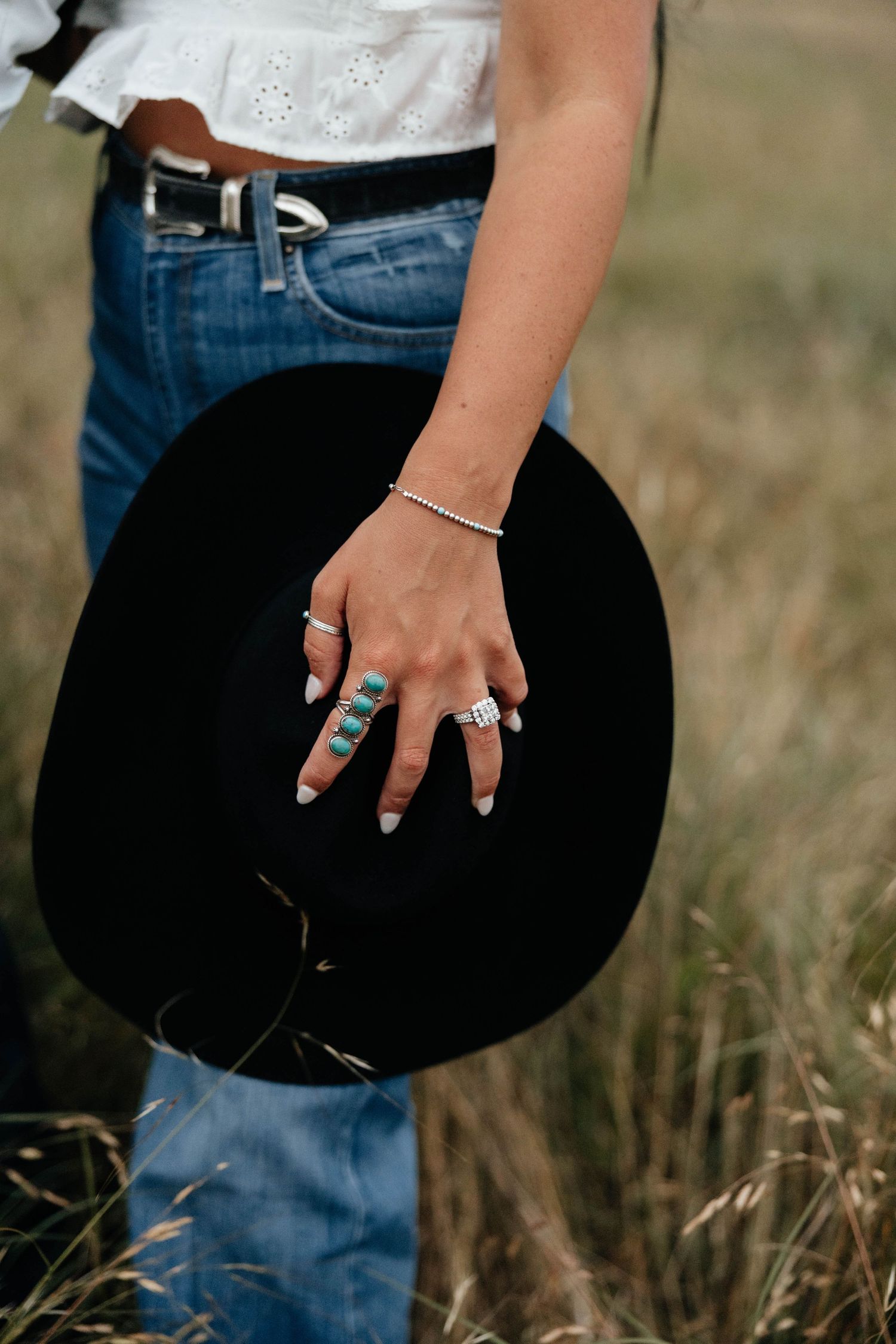 Close-up of woman's hand holding black cowboy hat, wearing turquoise rings, diamond ring, and silver bracelet.