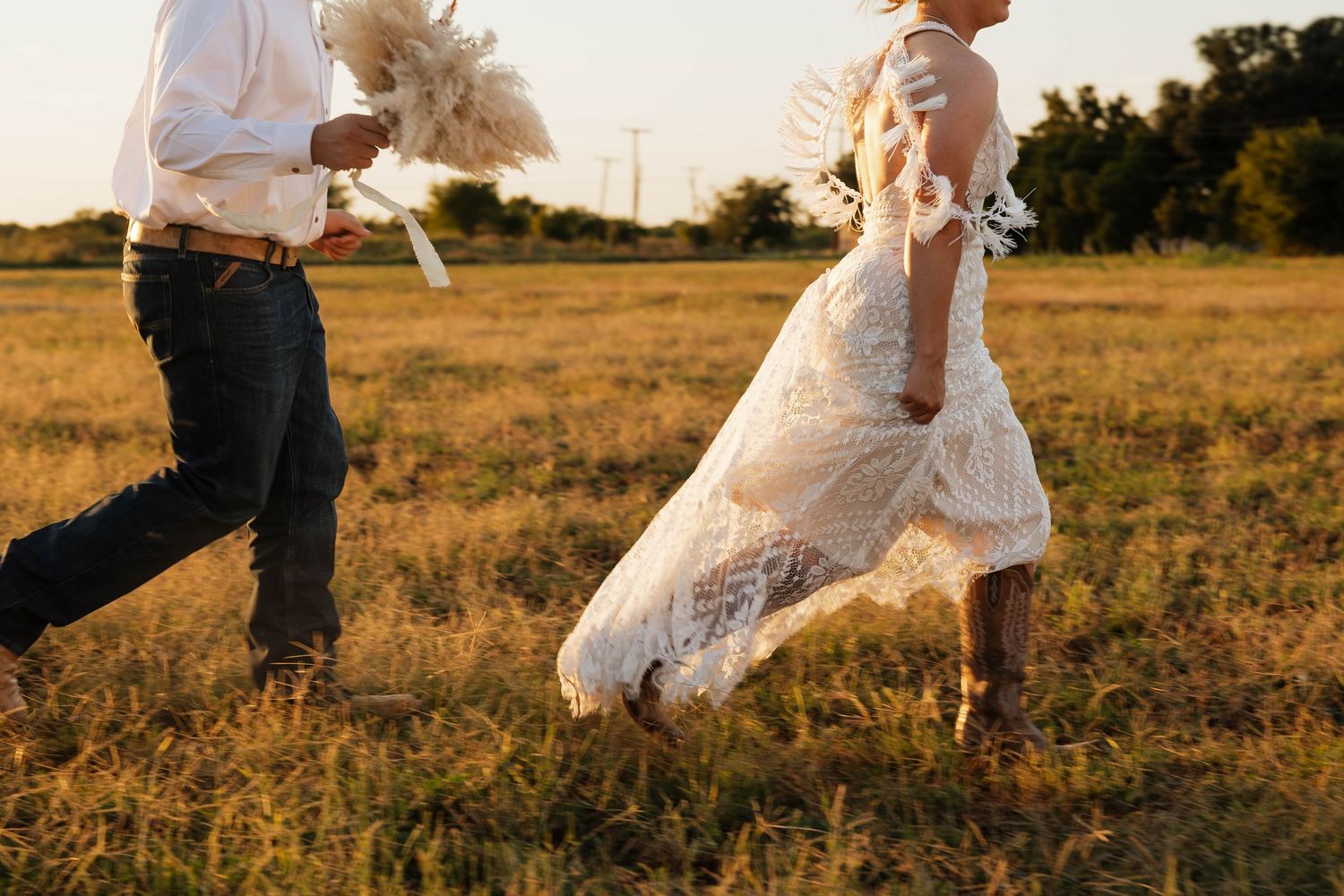 Bride and groom running joyfully through a sunlit golden field on their wedding day.