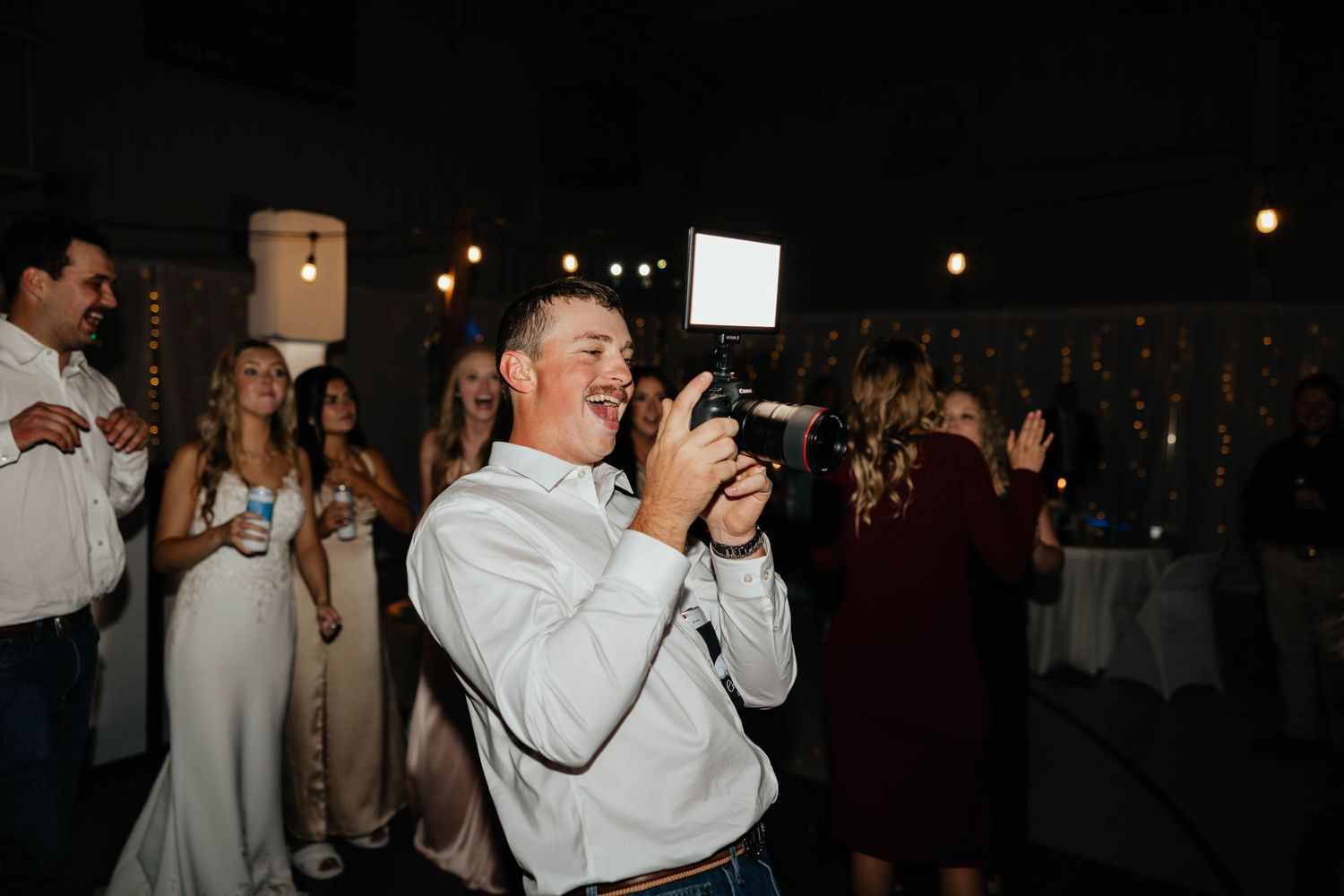 Guest photographing wedding reception celebration with professional camera under warm string lights.