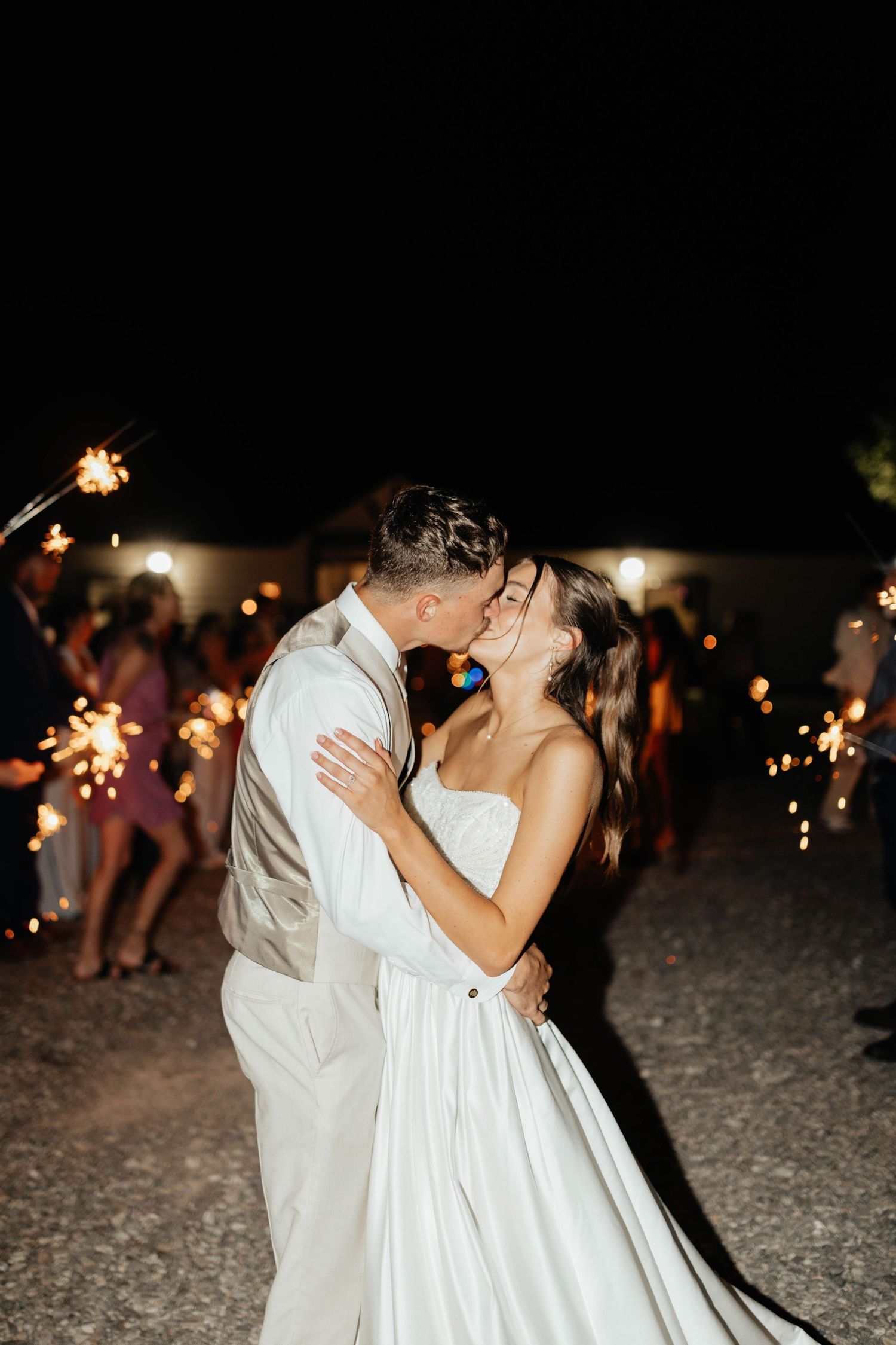Bride and groom share a passionate kiss surrounded by guests holding sparklers at their wedding reception.