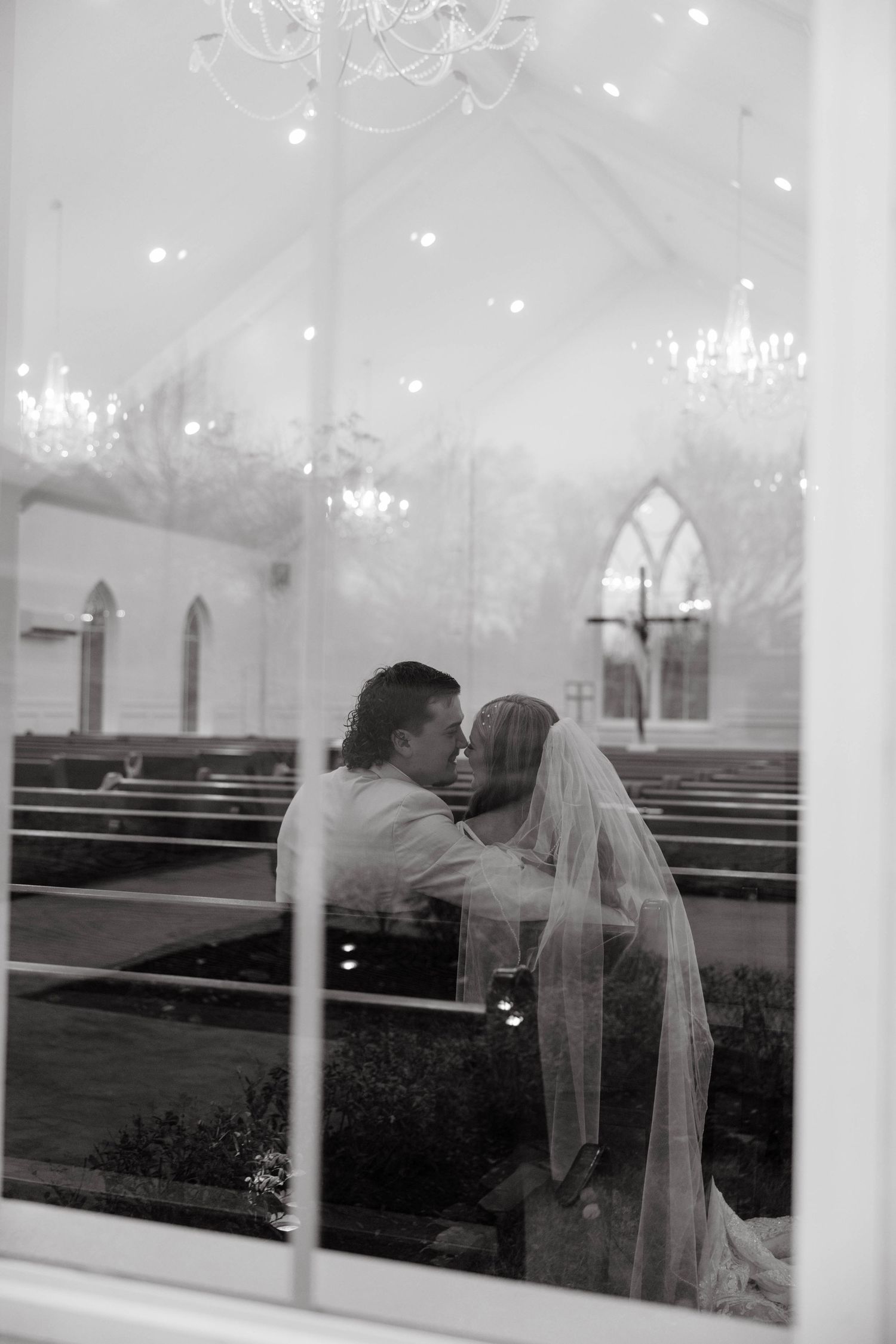 Black and white photo of bride and groom kissing inside an elegant chapel through glass.