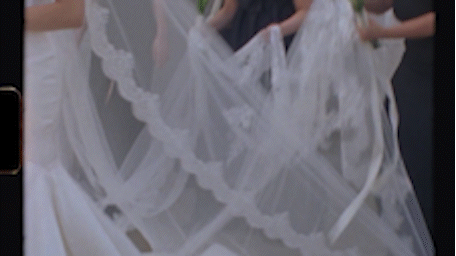 White wedding dress veil flowing in the wind, held by attendants during an outdoor bridal ceremony.