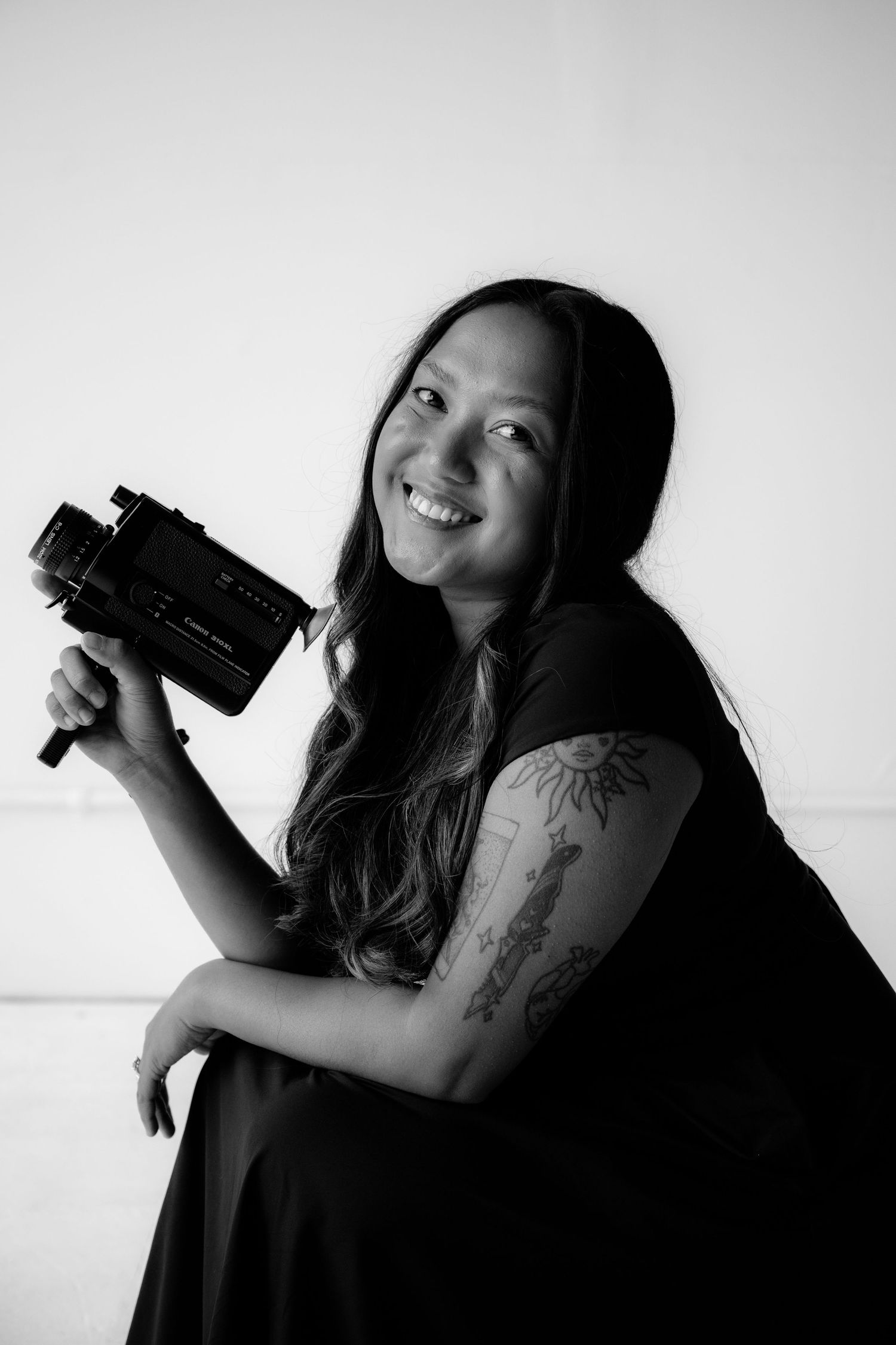 Black and white portrait of a photographer with long dark hair holding a camera and wearing a dark dress.