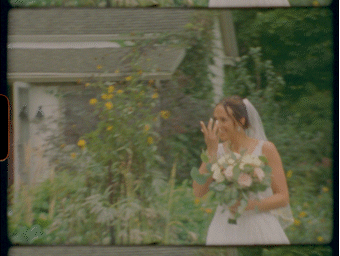 A bride in a white dress holds a bouquet while walking through a lush garden setting.