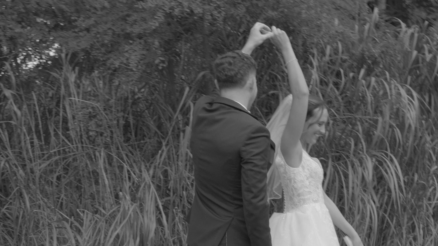 A couple dances gracefully in a field of tall grass during golden hour, creating a romantic silhouette.