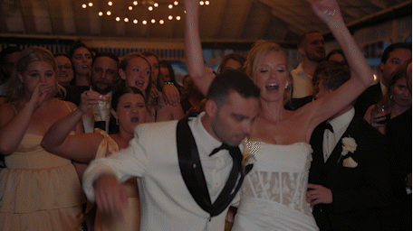 Joyful bride and groom celebrating at wedding reception with guests cheering in background.