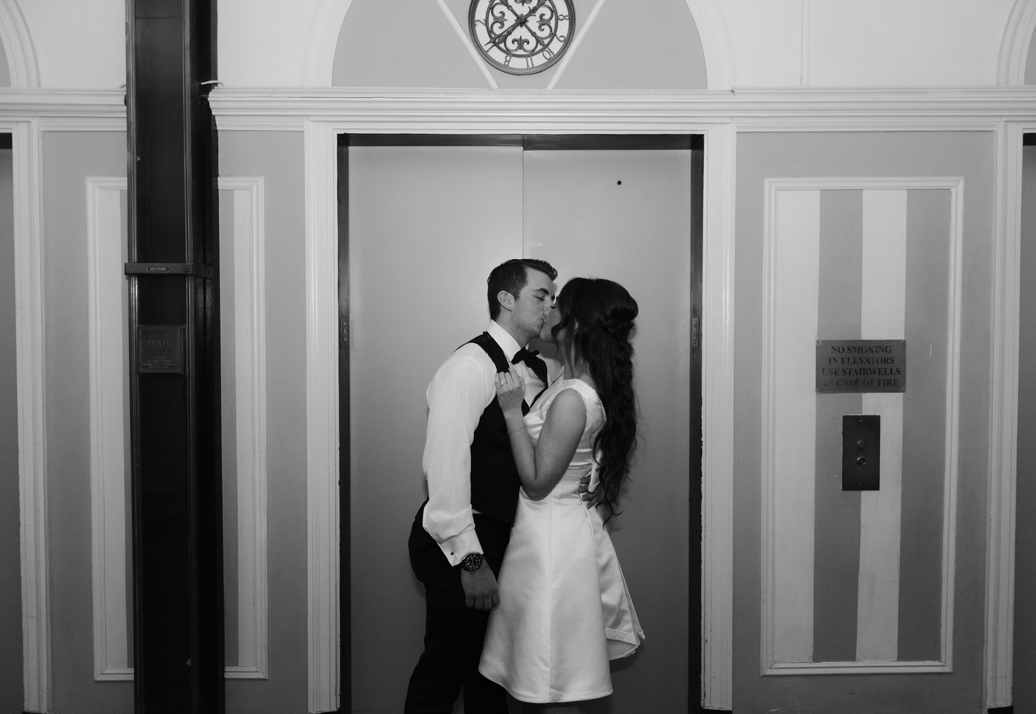 A romantic black and white photo of a couple sharing a kiss in front of an elevator door.