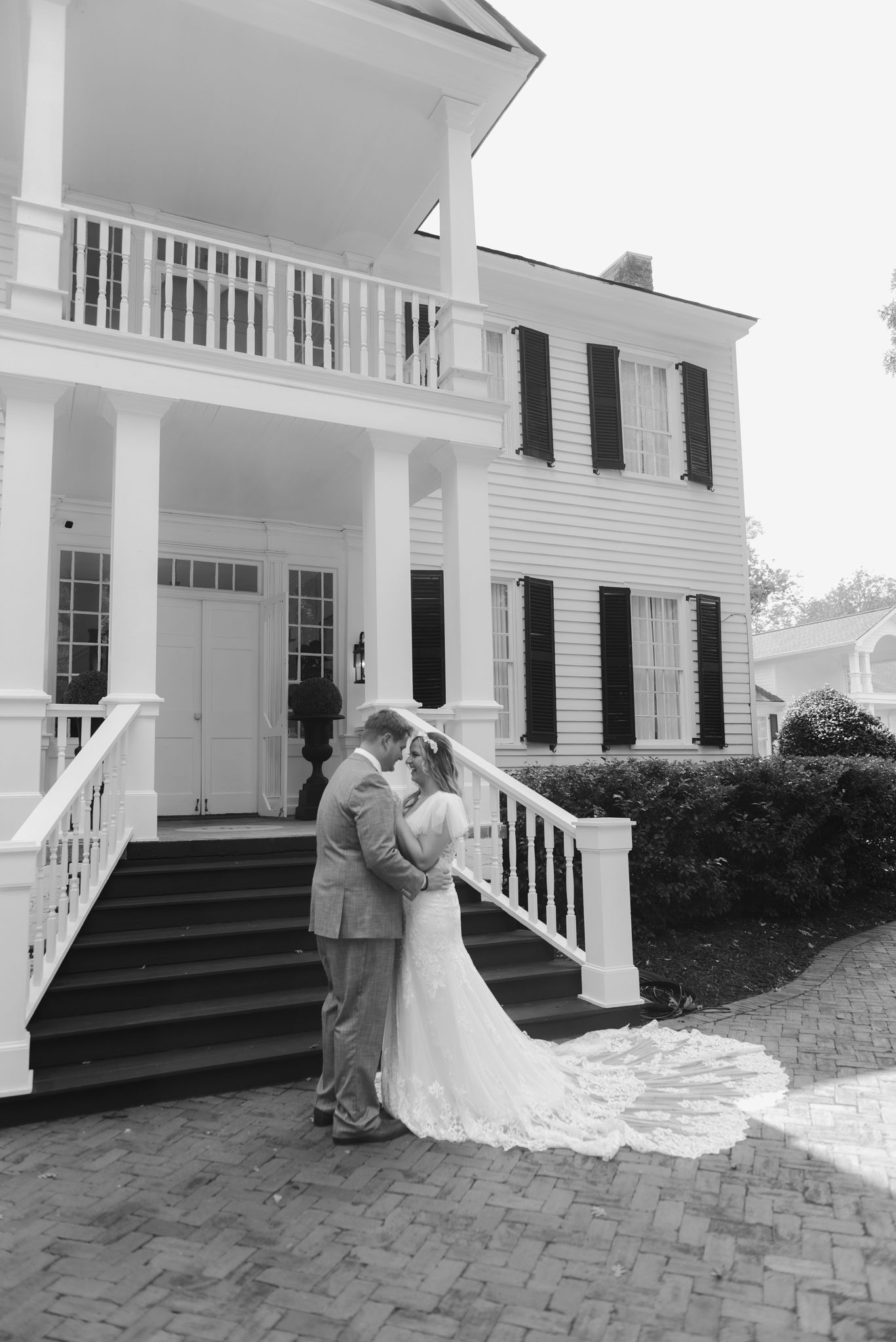 A couple shares their first dance outside a classic white colonial-style house.