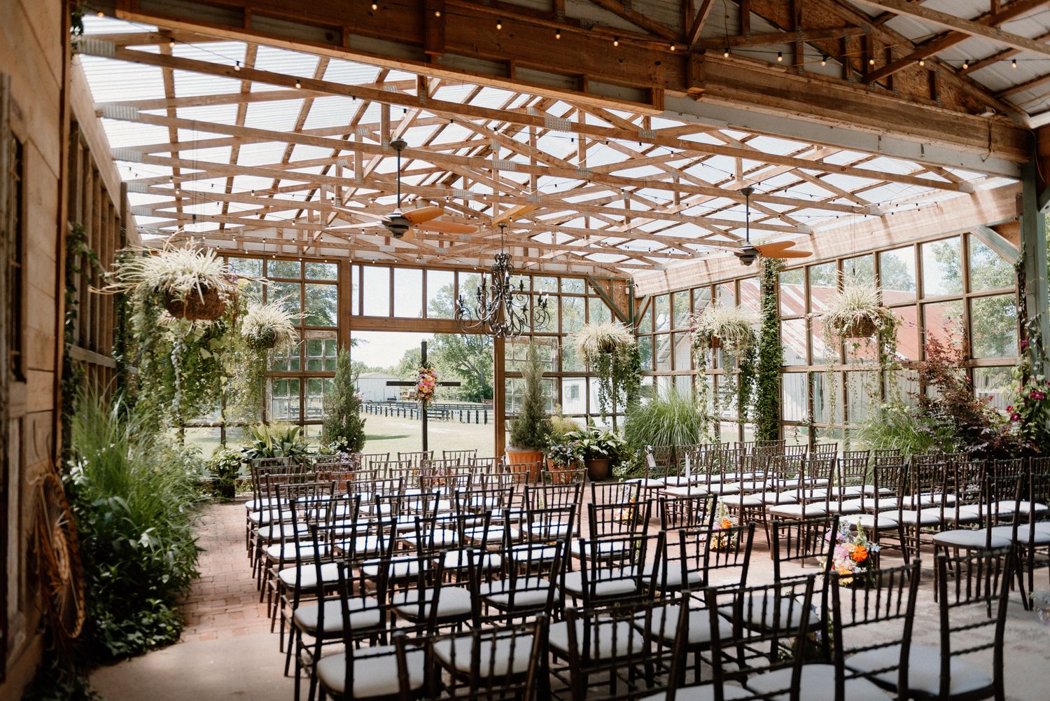 Indoor wedding ceremony setup with rows of chairs in a greenhouse-style venue with exposed wooden beams and natural light.