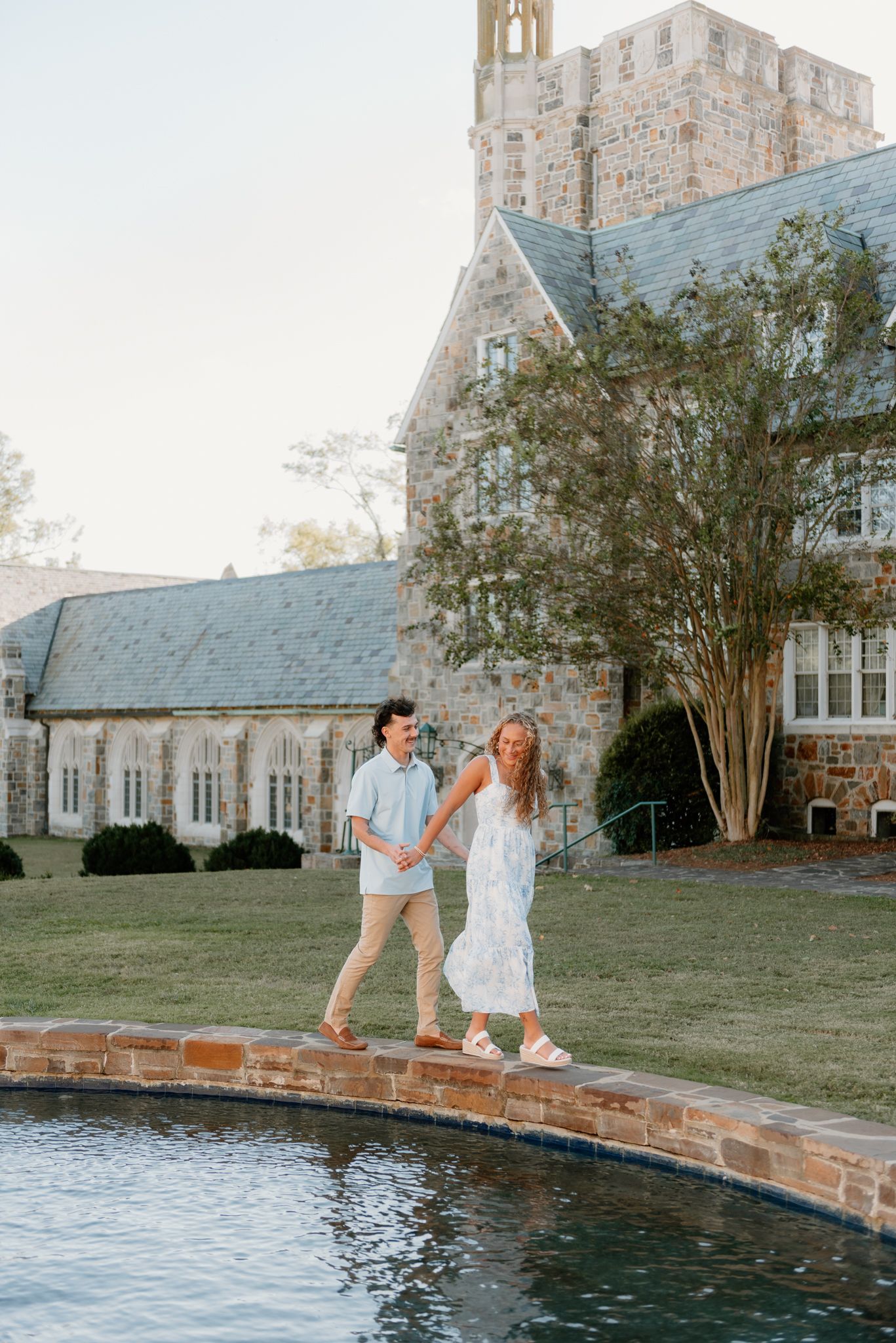 Couple relaxing by a stone-edged pond with Gothic church architecture in background.