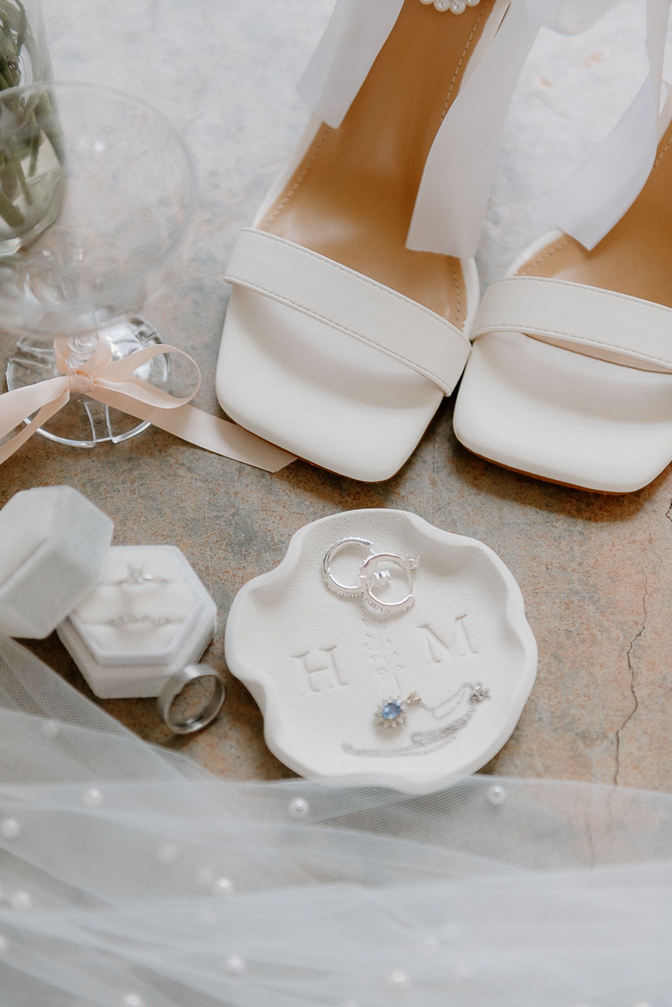 Wedding accessories flatlay with white shoes, ring dish, and wedding rings.