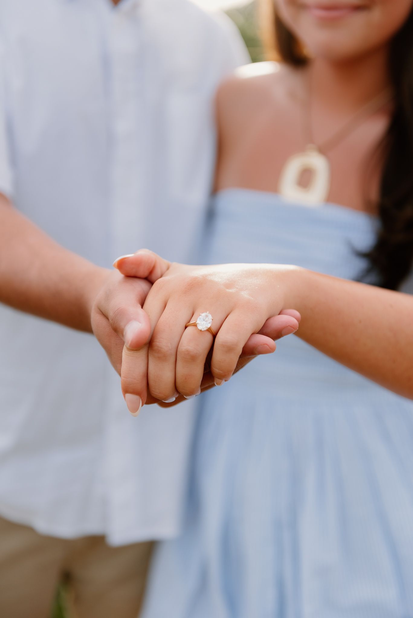 Close-up of hands showing an engagement ring against light blue fabric.