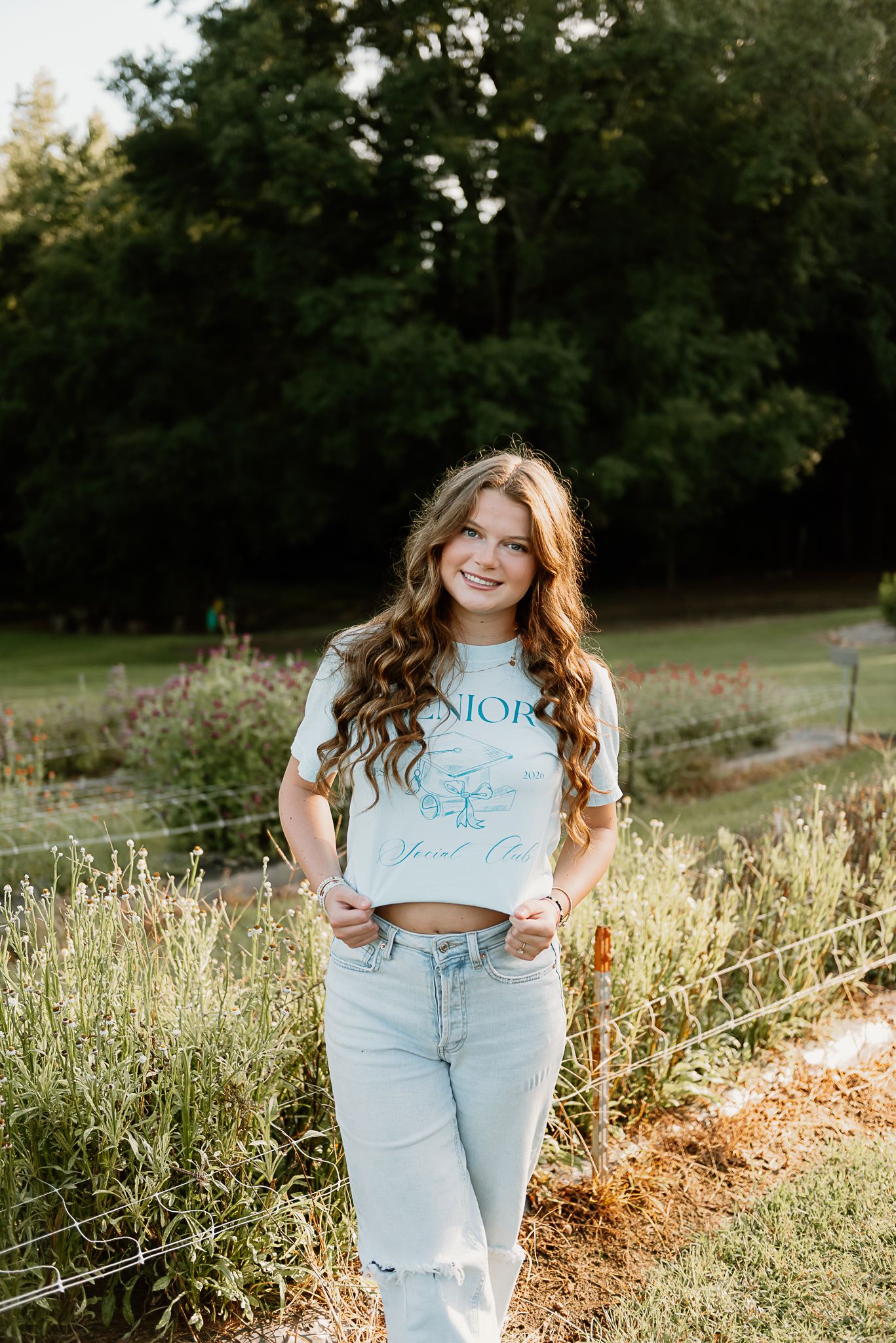 A person in ripped jeans and crop top poses in a sunlit field with wildflowers.
