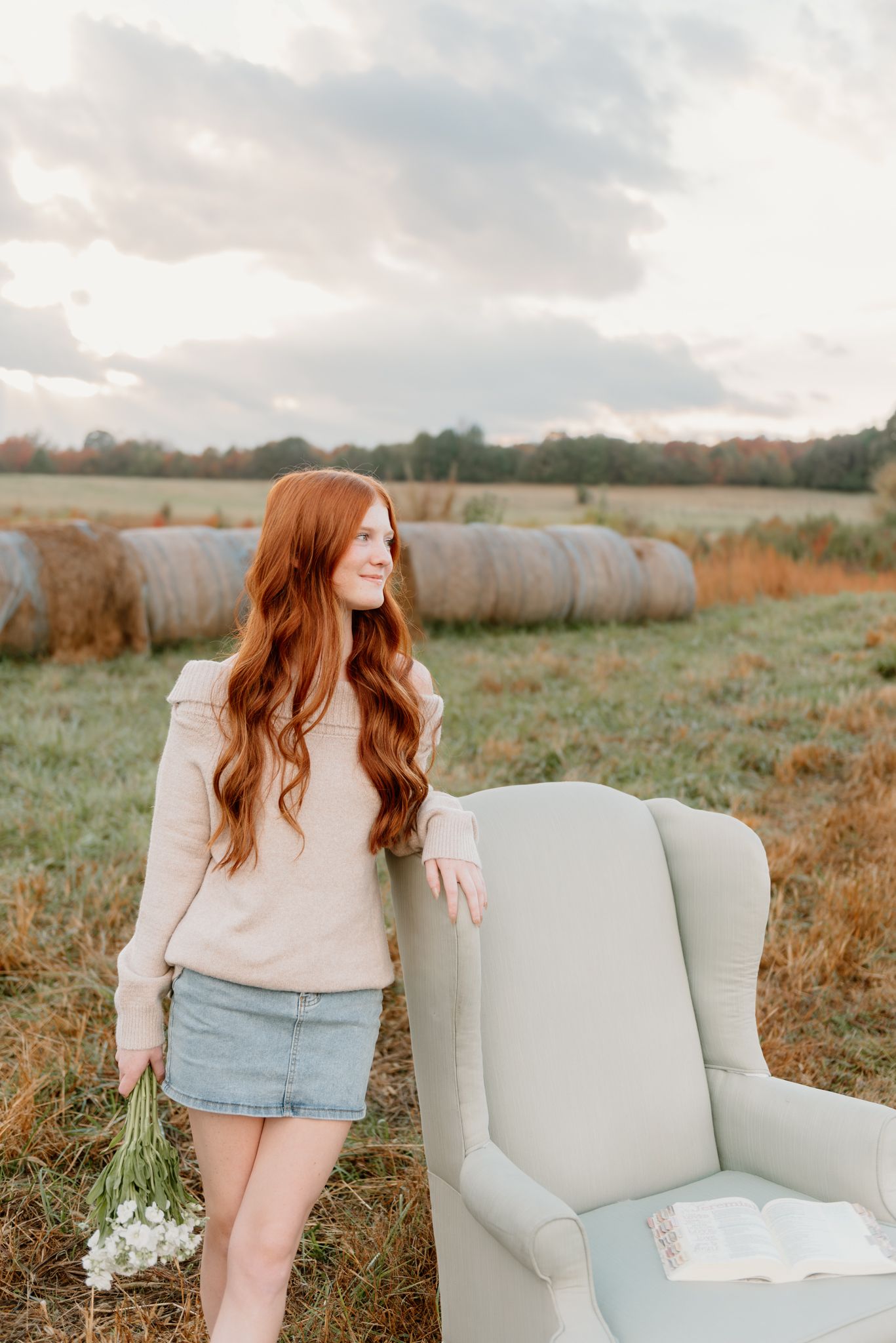 A vintage armchair sits in a rustic field during golden hour with autumn tones in the background.