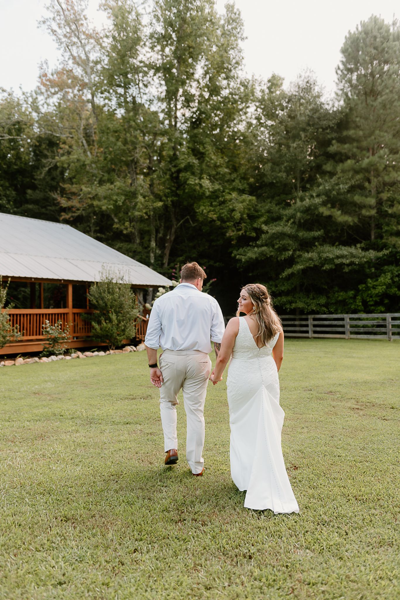 People walking across a grassy field towards a rustic cabin structure.