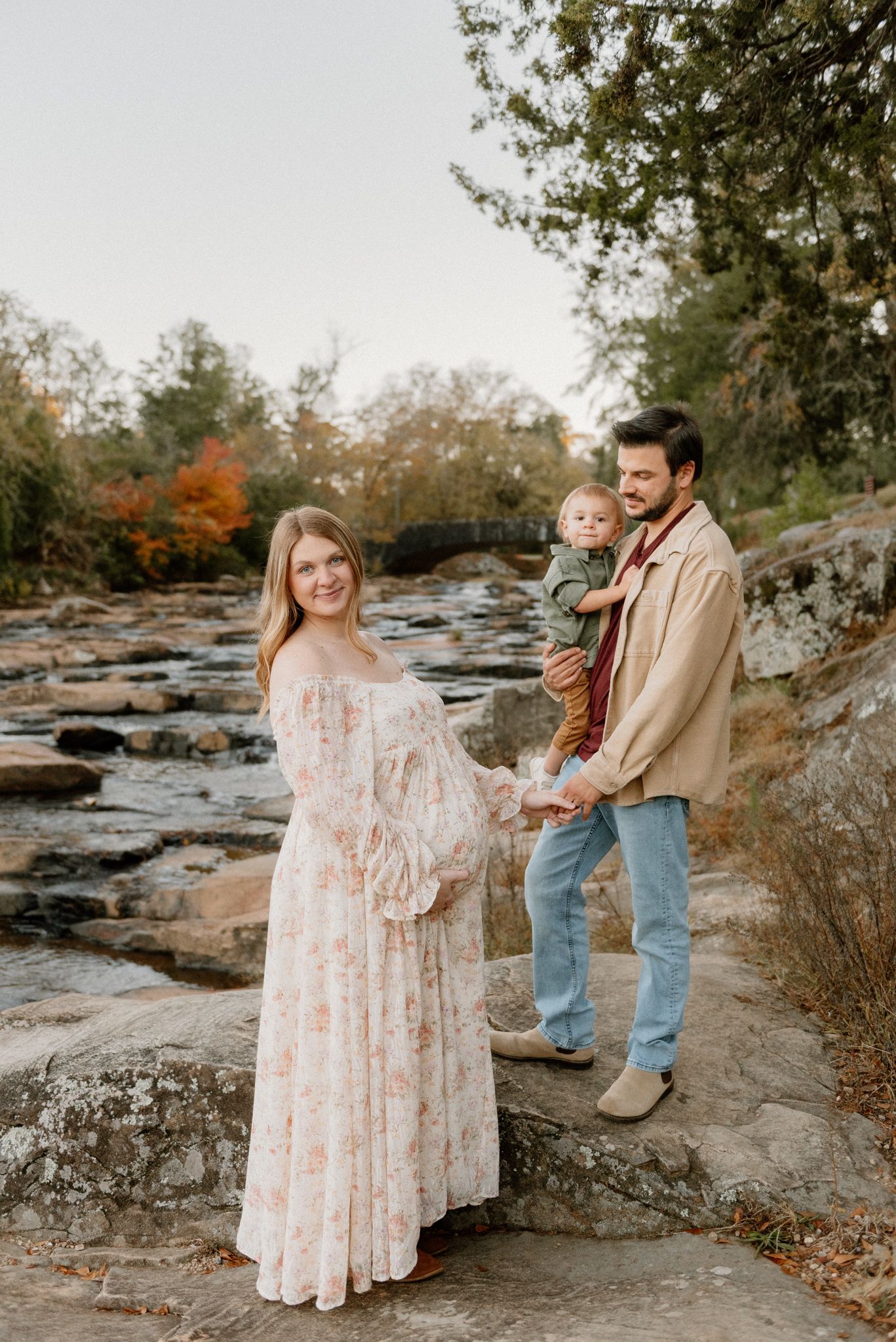A family enjoys a tender moment together on rocky terrain surrounded by autumn foliage.