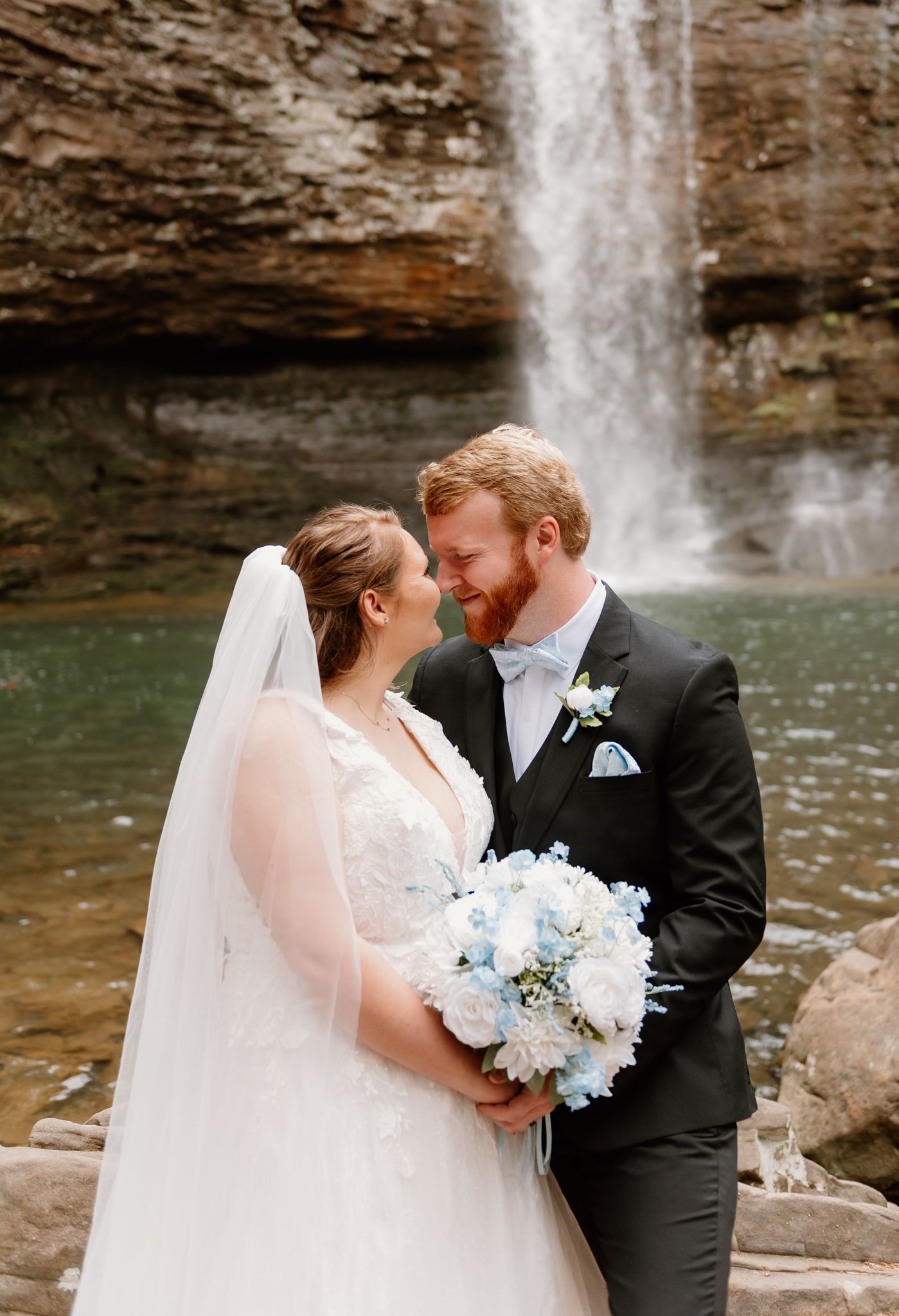 Newlyweds share an intimate moment in front of a cascading waterfall.