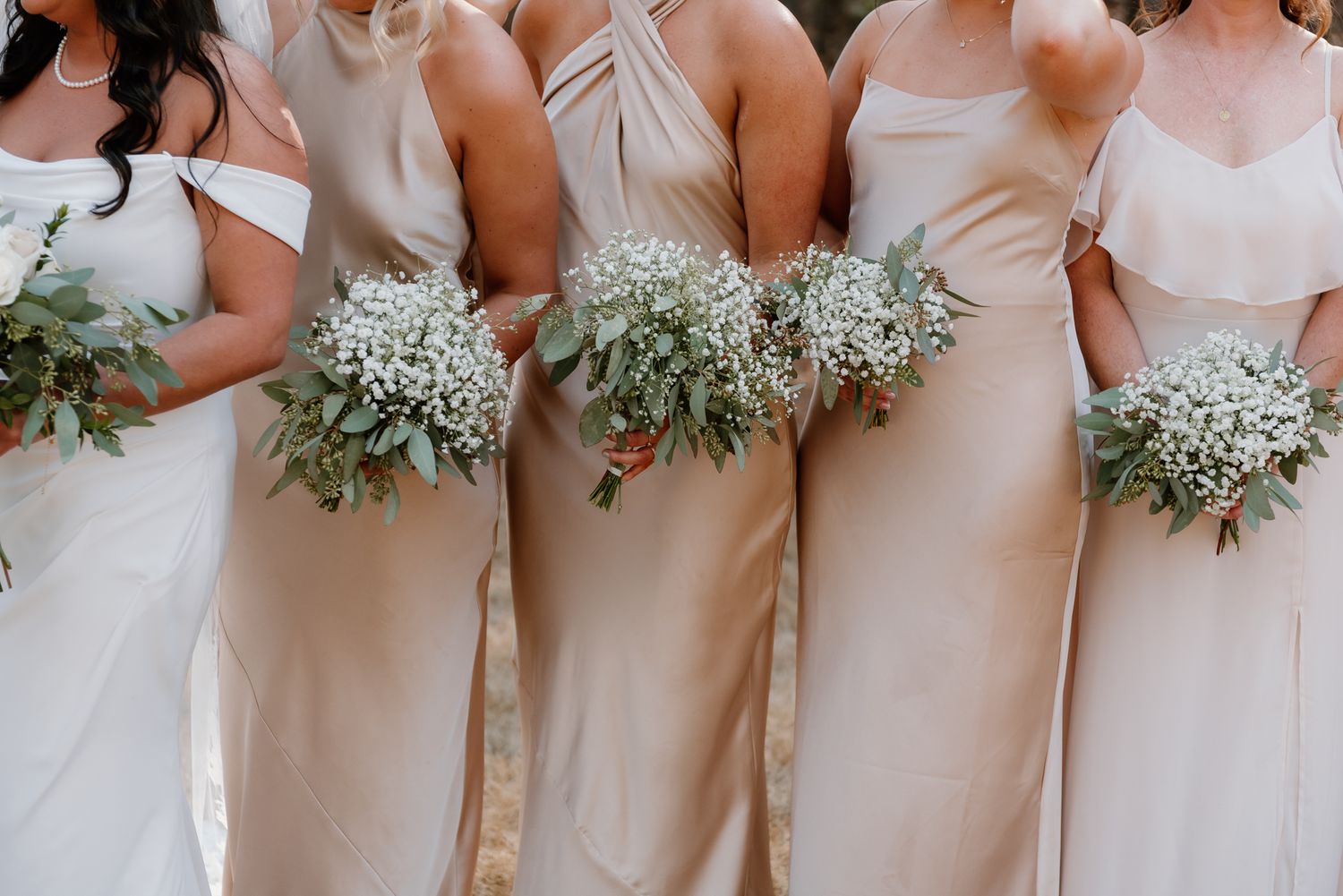 Bridesmaids in neutral dresses holding baby's breath bouquets.